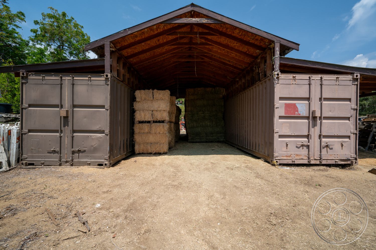 Ranch 6 - exterior, surrounding greenery, dirt floor, wood beam ceiling, straw bale storage, metal shipping containers, wooden roof with exposed rafters, rustic storage shed, open bay entrance