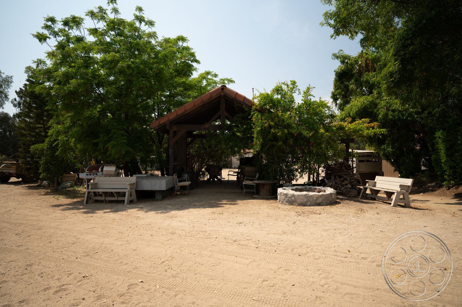 Ranch 6 - exterior, surrounding trees, outdoor dining area, terracotta roof tiles, wooden picnic tables, lush green landscaping, concrete fire pit, gravel outdoor flooring, wooden canopy structure, natural desert environment