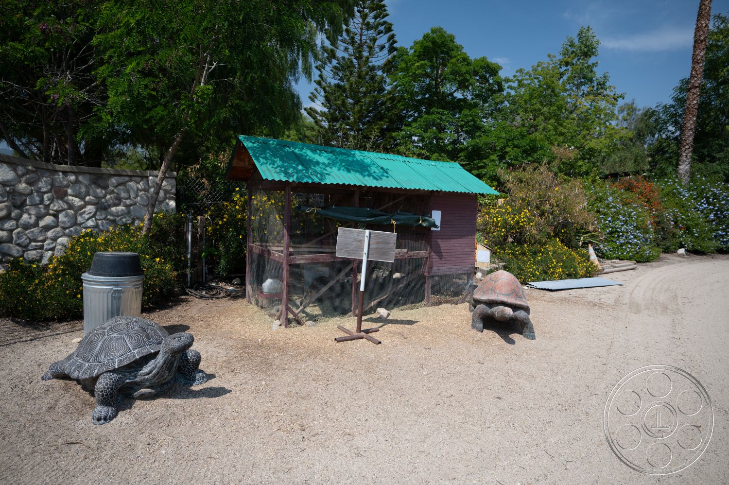 Ranch 6 - exterior, gravel pathway, flowering plants, wood fence, lush garden landscaping, stone garden wall, wooden birdhouse with green metal roof, decorative concrete turtle sculptures