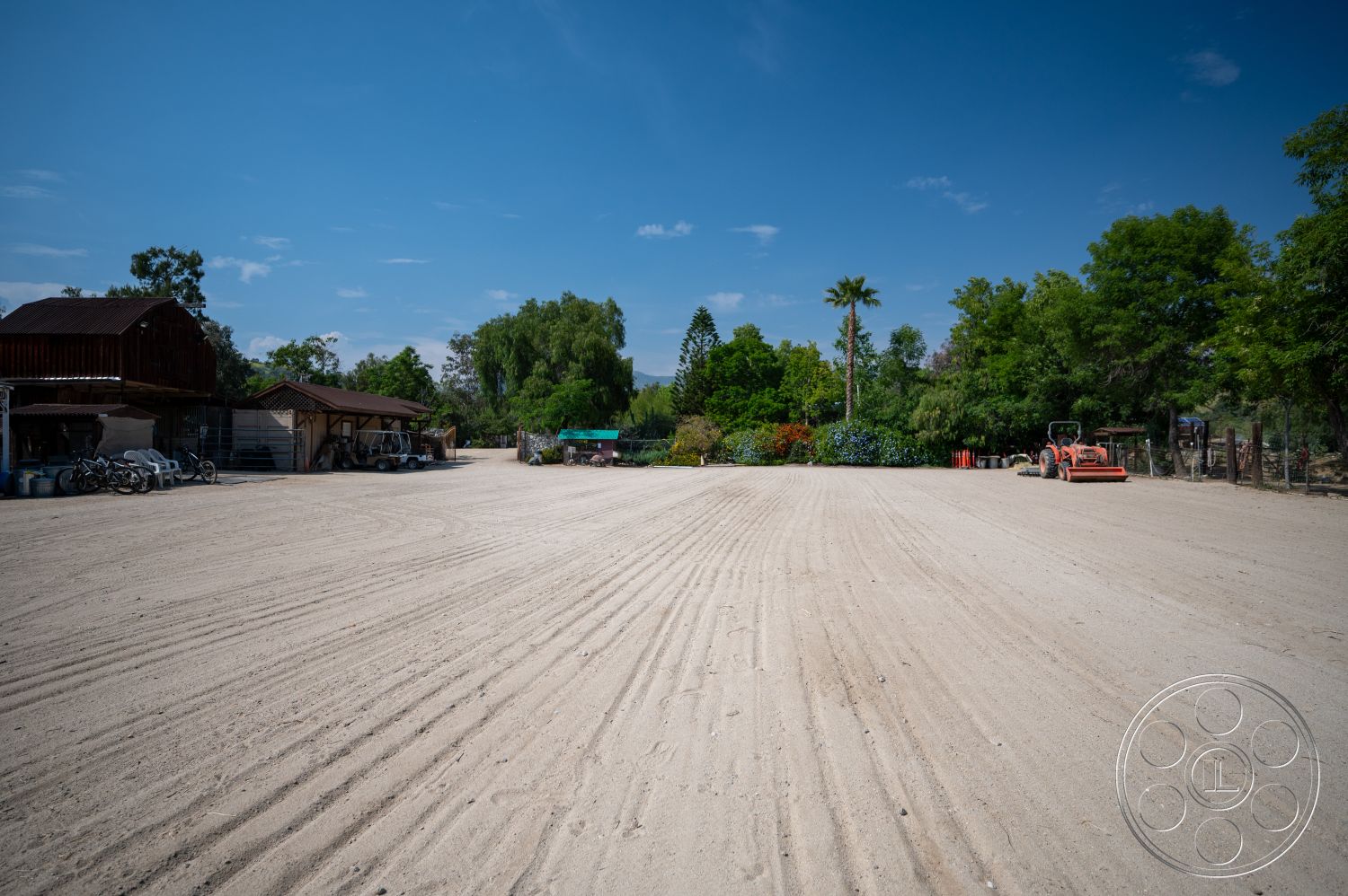 Ranch 6 - exterior, lush greenery, palm trees, sand surface, landscaped garden area, metal roof structure, gravel parking area, open agricultural setting, wooden barn style building, tractor parking space, outdoor equipment storage