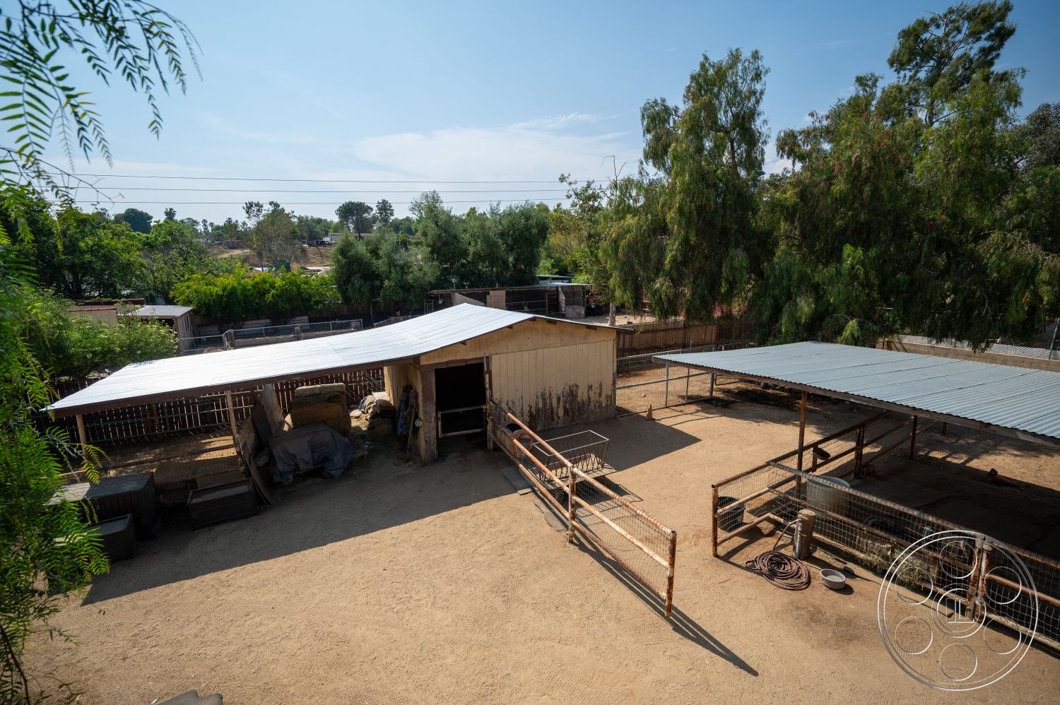 Ranch 6 - exterior, surrounding trees, metal roof, open sky, storage containers, wooden barn structure, rustic agricultural setting, outdoor animal pens, dirt ground surface, fenced livestock area, shade awning
