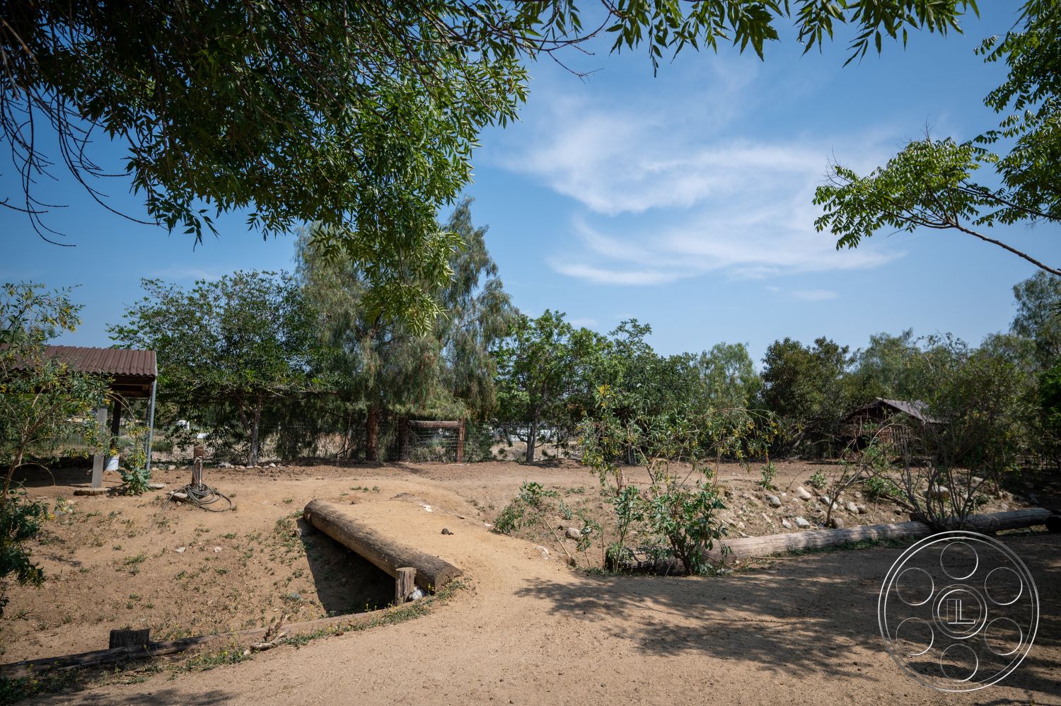 Ranch 6 - exterior, wooden fence, wooden bridge, dirt pathway, sandy terrain, native vegetation, landscaped garden area, metal roof structure, natural ground cover, outdoor landscape setting