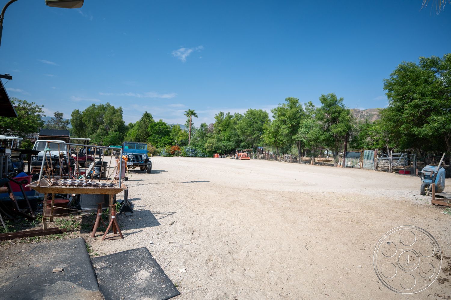 Ranch 6 - open space, surrounding trees, wooden table, outdoor setting, vintage vehicles, sunny outdoor environment, gravel ground surface, dirt yard