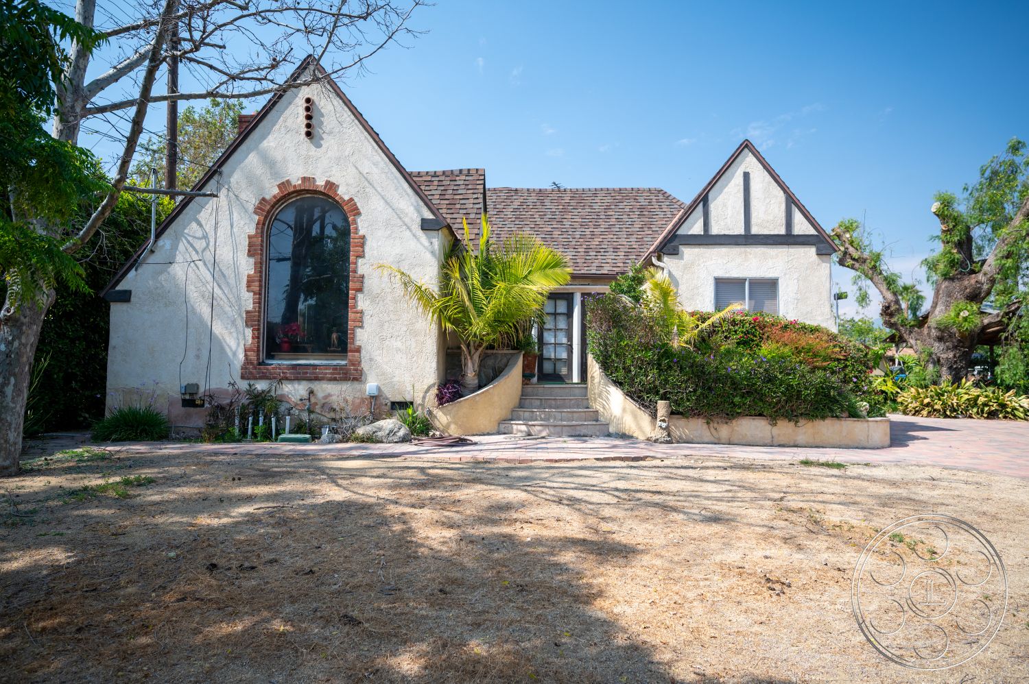 Ranch 6 - exterior, landscaped garden, asphalt shingle roof, wooden door, gabled roof, tropical landscaping, arched windows, traditional architectural style, stepping stone pathway, decorative eaves, stucco house facade, brick window trim, paved front patio