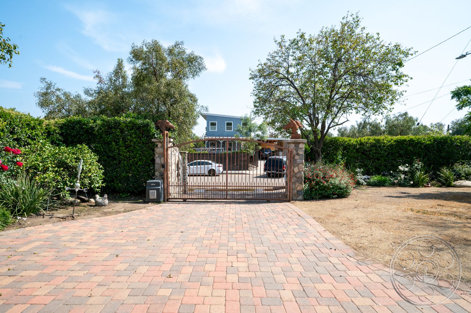 Ranch 6 - exterior, landscaped garden, paver driveway, metal gate, flowering plants, residential setting, hedge fencing, gravel ground cover, brick paver driveway, trees surrounding property, stone entry gate