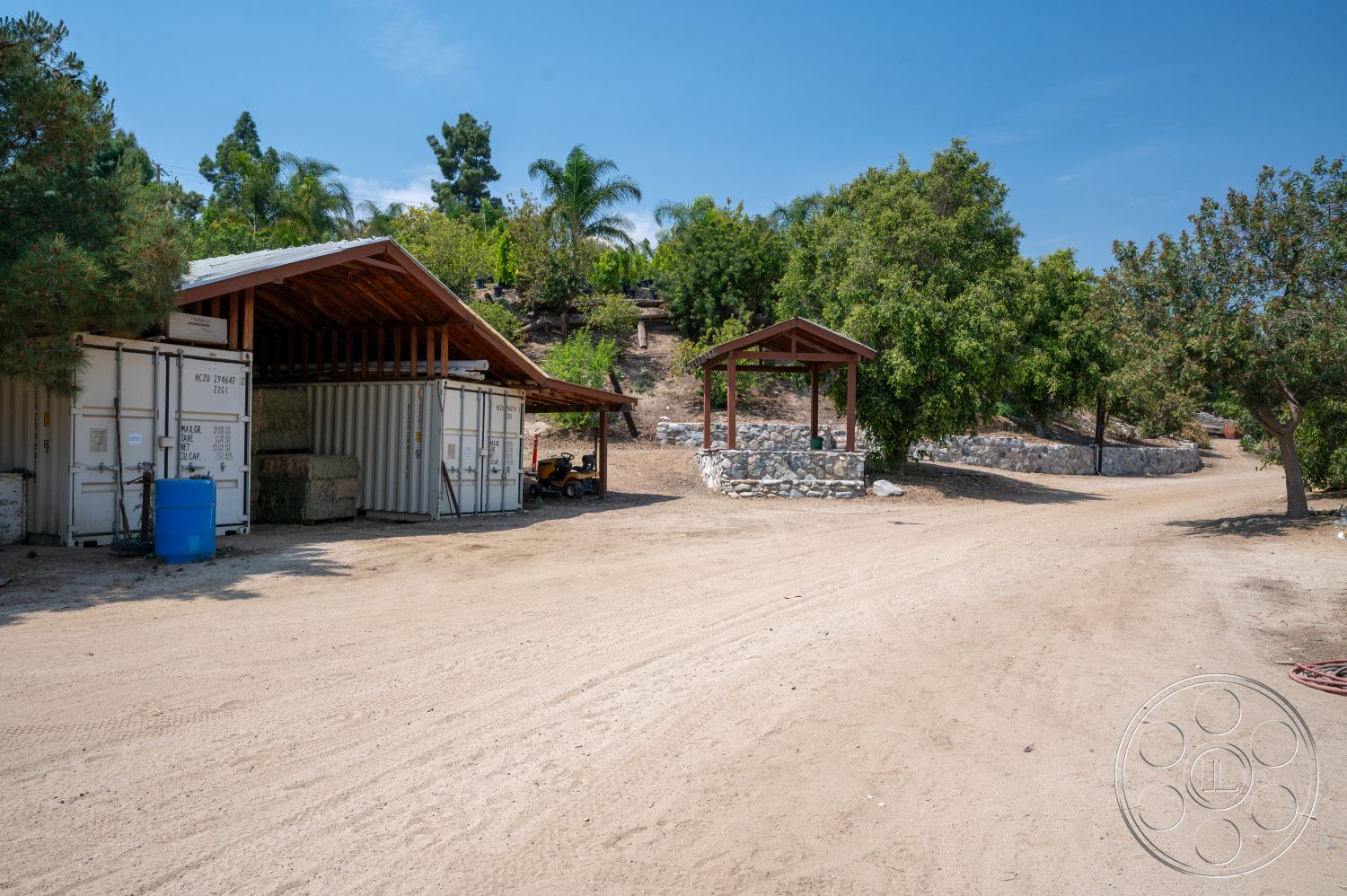 Ranch 6 - exterior, rural setting, stone retaining wall, open sky, landscaped garden with trees, exposed wooden rafters, metal storage containers, wooden post gazebo, dirt access road