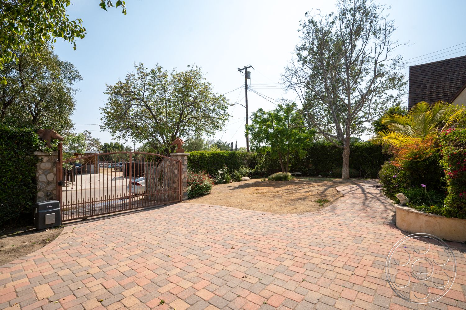 Ranch 6 - paved driveway, deciduous trees, sunny outdoor setting, evergreen shrubs, landscaped garden area, stone boundary wall, brick driveway pavers, exterior gate