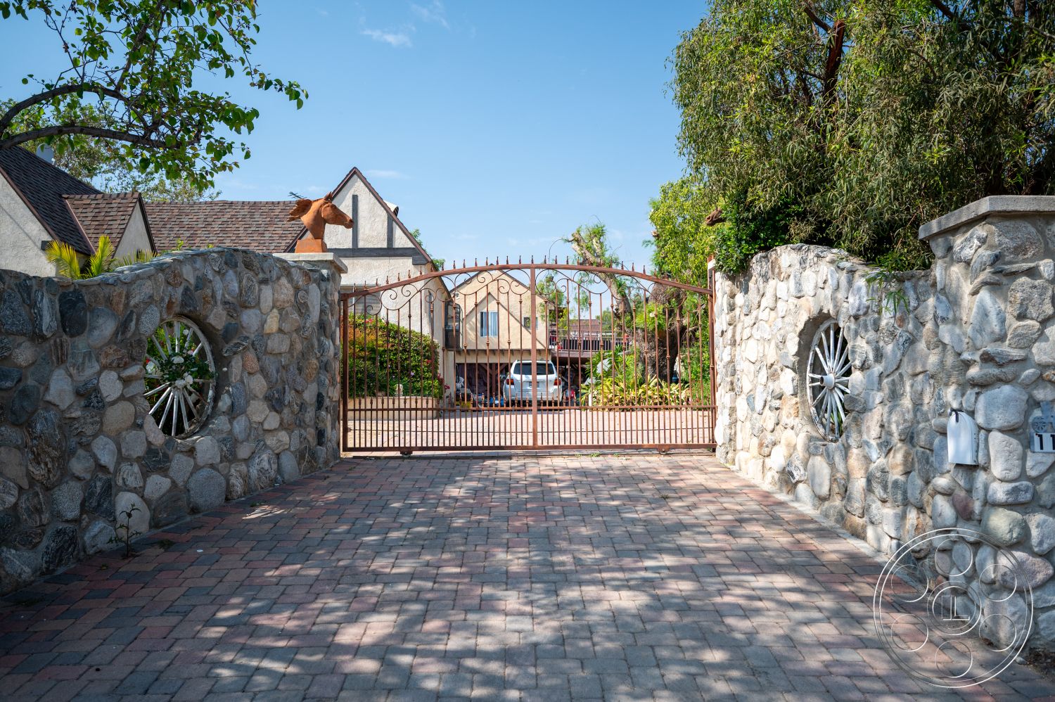 Ranch 6 - exterior, landscaped garden, gabled roof, tree line, residential entrance, wrought iron gate, wood beam accents, brick driveway pavers, stone garden wall, round stone feature wall, stone entryway