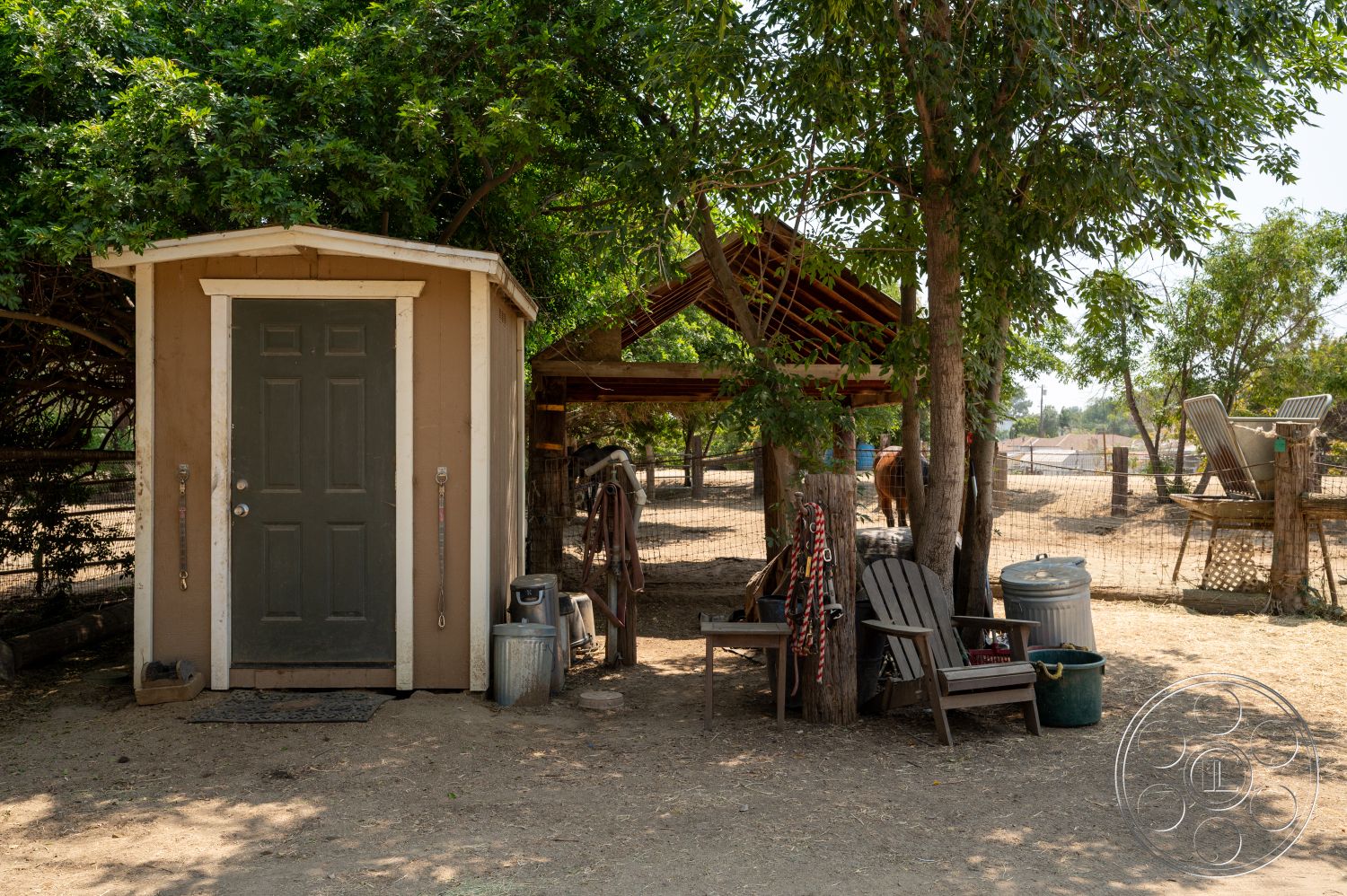 Ranch 6 - exterior, fenced area, shade from trees, green door, wooden outdoor seating, wooden shed structure, metal trash can, dirt ground surface, simple outdoor shelter, rustic farmland setting