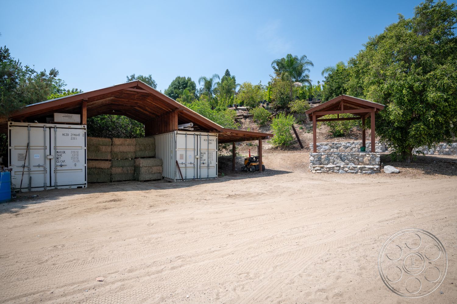 Ranch 6 - exterior, suburban setting, landscaped hillside, wooden gazebo, stone wall feature, gravel ground surface, outdoor storage area, hay bale storage, wooden roof structure, metal shipping containers
