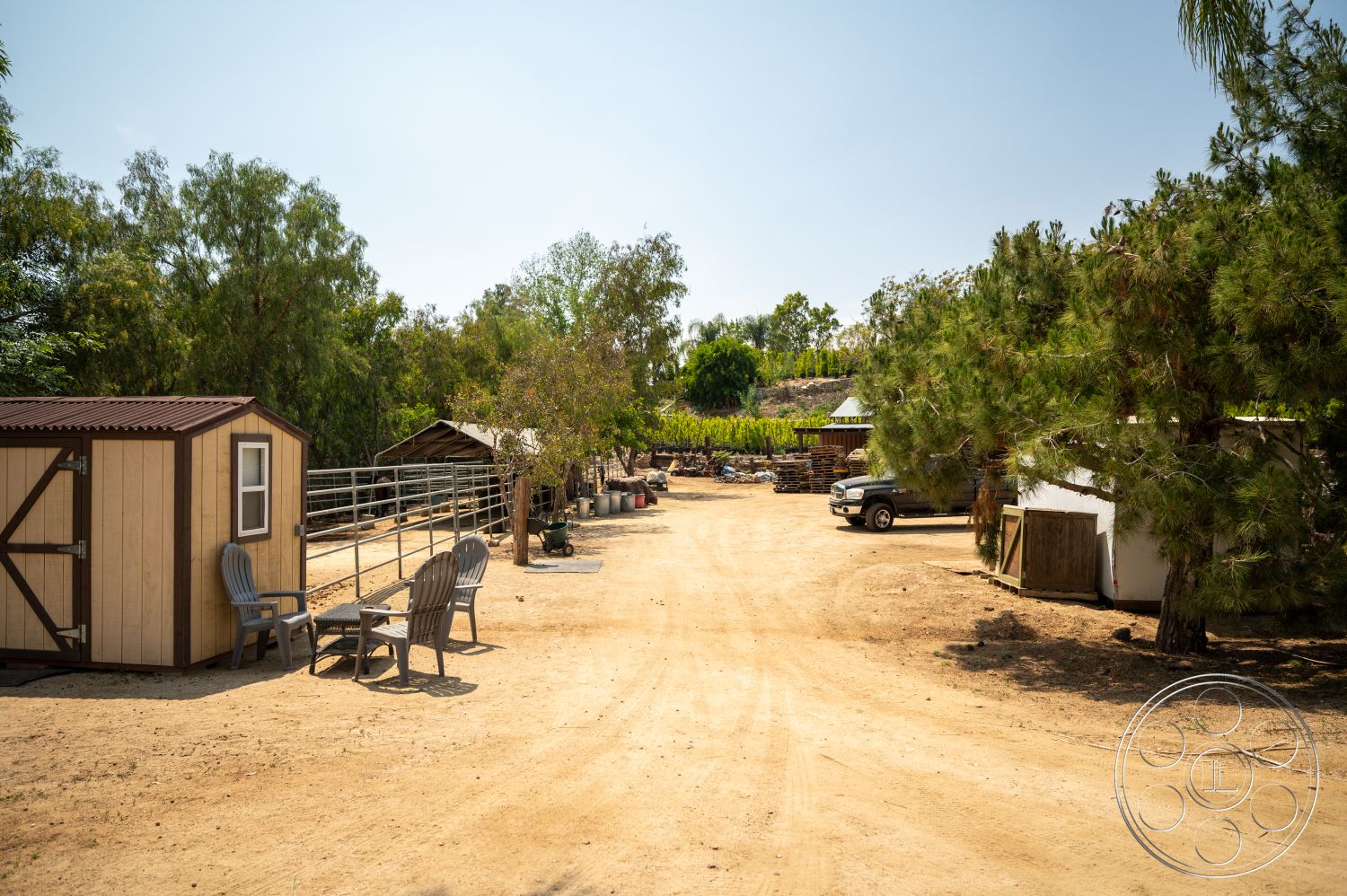 Ranch 6 - exterior, wooden shed, dirt driveway, metal roofing, rural farmhouse setting, wooden fence panels, landscaped garden with trees, seating area with outdoor chairs, surrounding vineyard