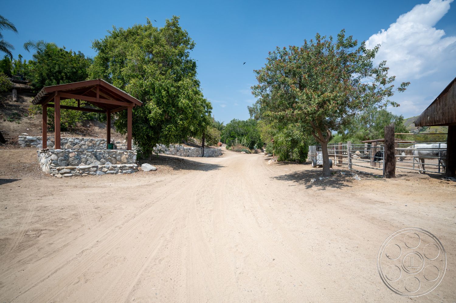 Ranch 6 - exterior, mature trees, natural stone wall, dirt driveway, hillside location, landscaped garden area, open rural setting, wooden gazebo with slanted roof, rustic wooden fencing, fenced horse area