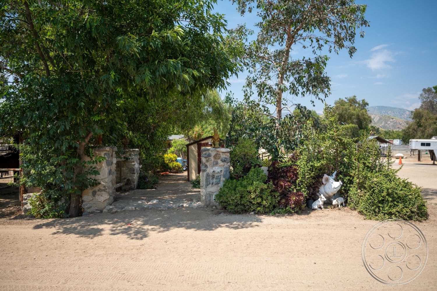 Ranch 6 - lush greenery, gravel pathway, outdoor setting, eucalyptus trees, landscaped garden area, stone entrance pillars, rustic gate, semi-rural environment