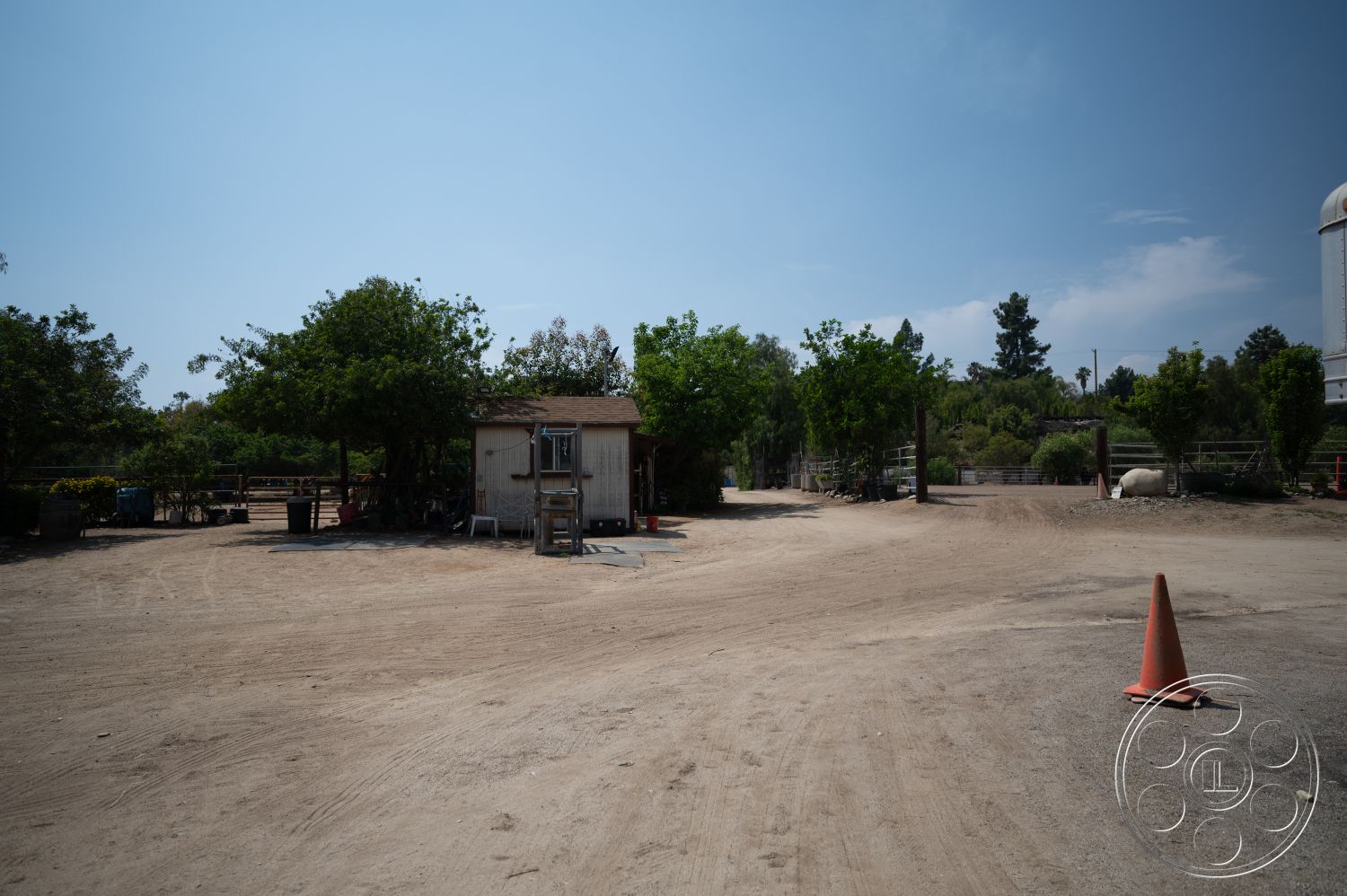 Ranch 6 - exterior, lush greenery, blue sky, wooden shed, ornamental trees, dirt driveway, open field, gravel surrounding, orange construction cone
