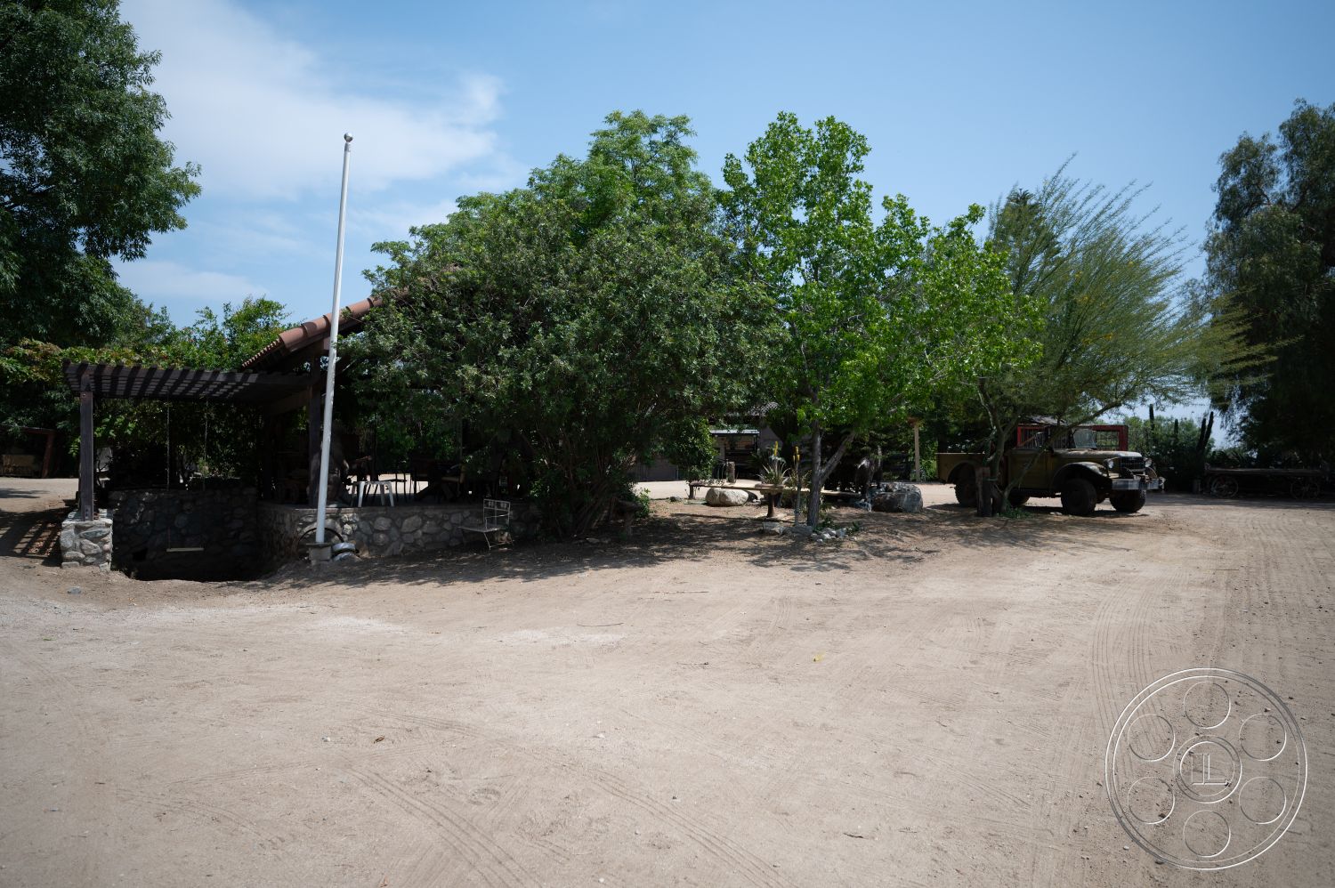 Ranch 6 - exterior, lush greenery, open outdoor space, wood pergola structure, rustic outdoor setting, patio dining area, dirt landscaping, stone wall base, parked vintage military vehicle, natural shaded area