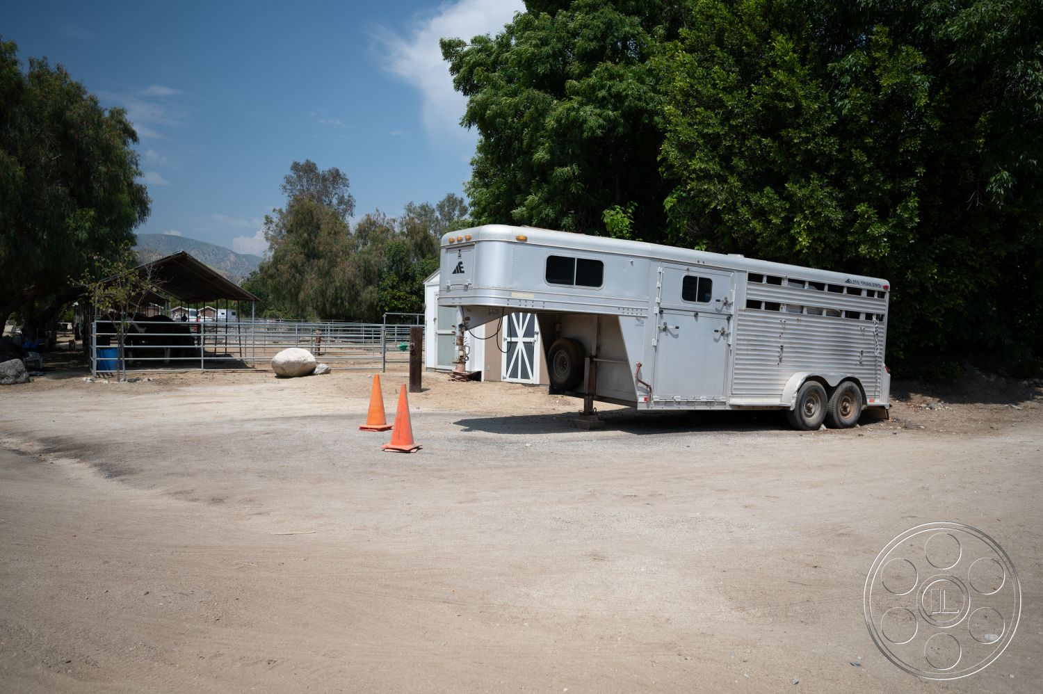 Ranch 6 - exterior, surrounding trees, rural setting, scattered rocks, safety cones, metal horse trailer, hay storage area, silver aluminum cladding, two-axle trailer, dirt parking surface