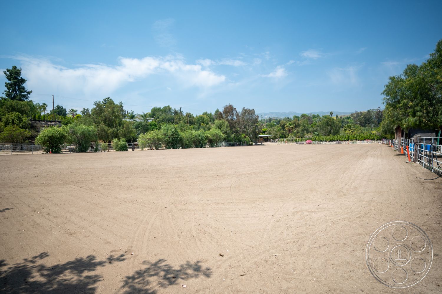 Ranch 6 - exterior, surrounding greenery, clear blue sky, distant mountain view, tree-lined perimeter, sand riding arena, fenced equestrian area