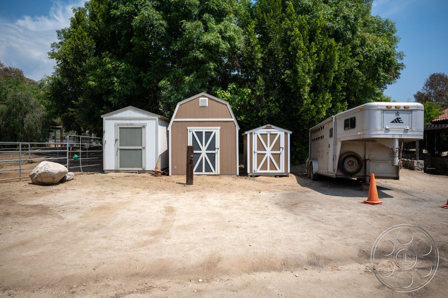 Ranch 6 - exterior, surrounding greenery, gabled roof, orange traffic cone, white painted walls, wooden storage shed, rustic rural setting, metal horse trailer, brown wood accent details, dirt surface