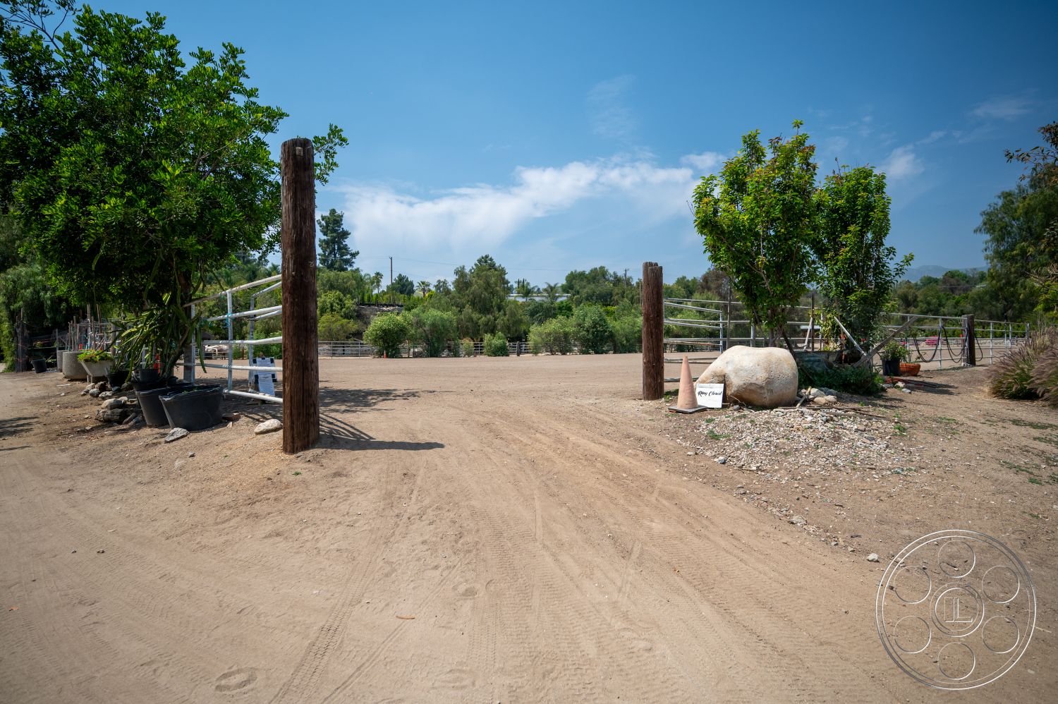 Ranch 6 - outdoor space, natural landscaping, green foliage, landscape plants, clear blue sky, rural setting, dirt pathway, rocky ground, wooden fence posts, rustic entrance