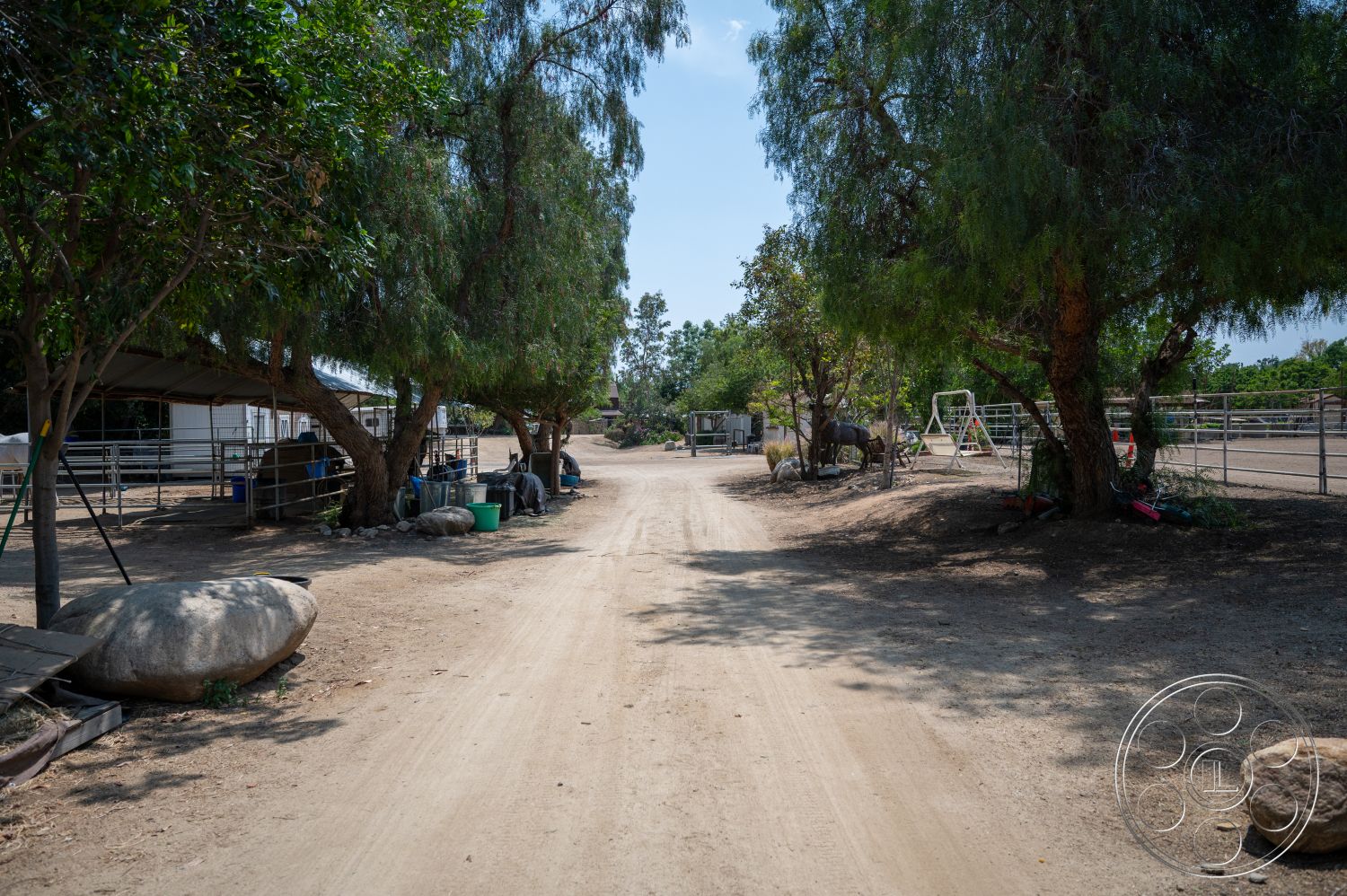 Ranch 6 - open space, surrounding trees, rural setting, agricultural landscape, sunlit outdoor environment, fenced pasture area, dirt access road, exposed rock boulders, stable structures