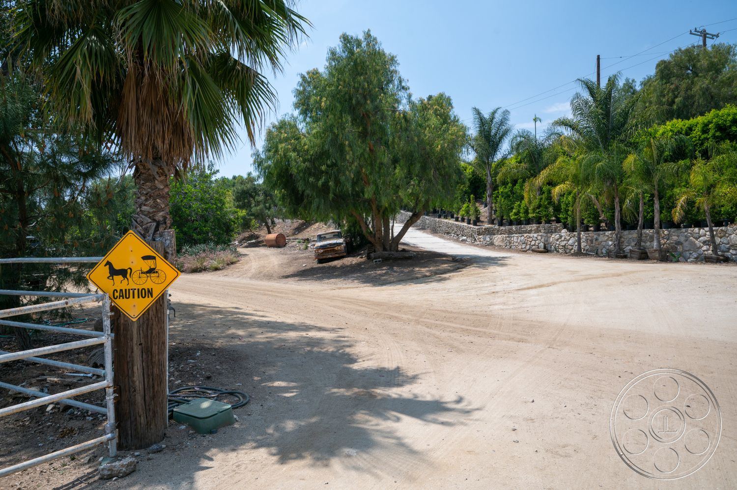 Ranch 6 - exterior, palm trees, green shrubbery, outdoor setting, dirt driveway, stone retaining wall, rural landscape, wooden gate post, caution sign