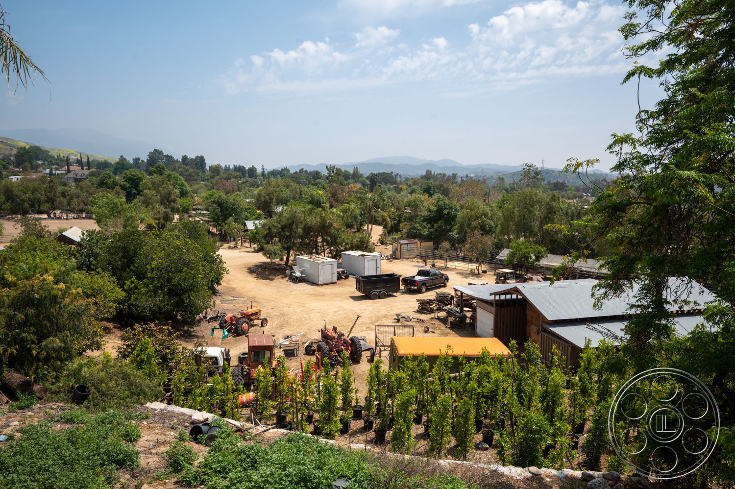 Ranch 6 - exterior, mountain view, metal roof shed, wooden barn structure, open field area, rustic agricultural setting, dirt yard, gravel farm road, farm equipment storage area, landscaped garden with vines, tree line border, roadside pickup trucks