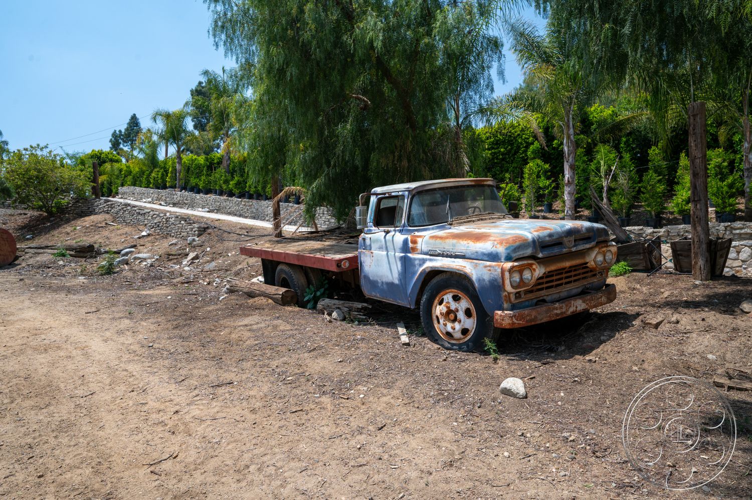 Ranch 6 - exterior, gravel ground, stone retaining wall, dry terrain, surrounding palm trees, landscaped shrubbery, wooden fence posts, temporary storage area, dirt landscape, rusty vintage truck, weathered blue paint