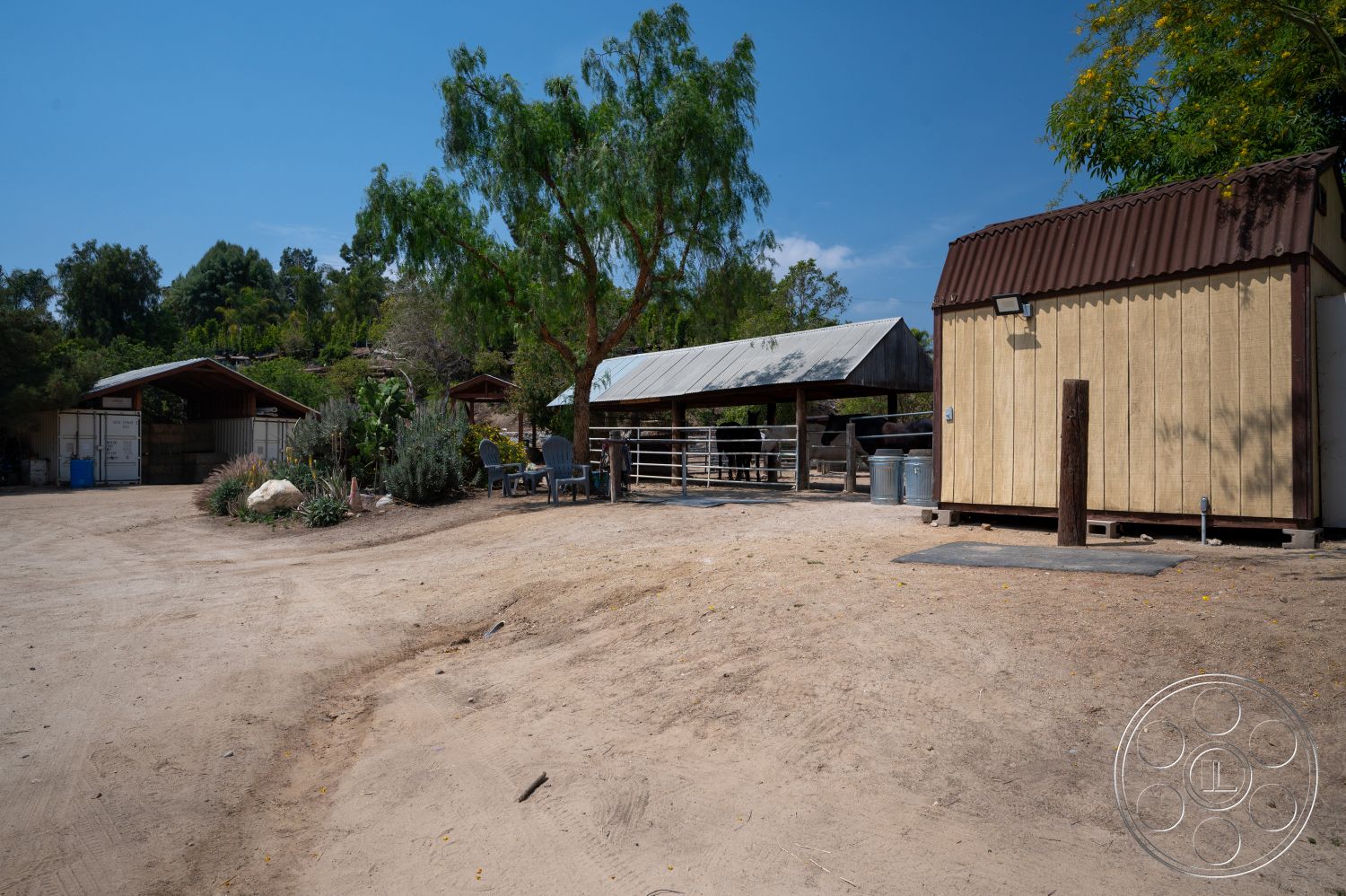 Ranch 6 - outdoor seating area, gravel landscaping, dirt driveway, agricultural setting, wooden fencing, natural foliage, metal roofed barn, rustic outbuilding, open horse corral, exterior rustic design