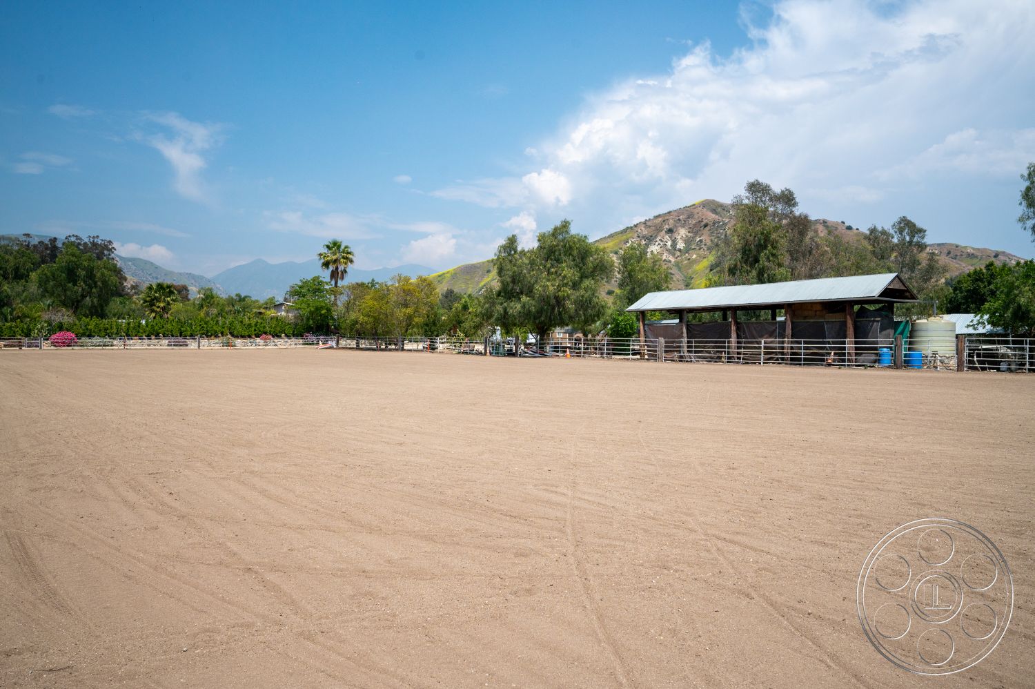 Ranch 6 - exterior, metal roof, fenced pasture, drought-resistant landscaping, surrounding mountain landscape, wooden stable structure, dusty sand riding arena, palms trees, scenic hills in background