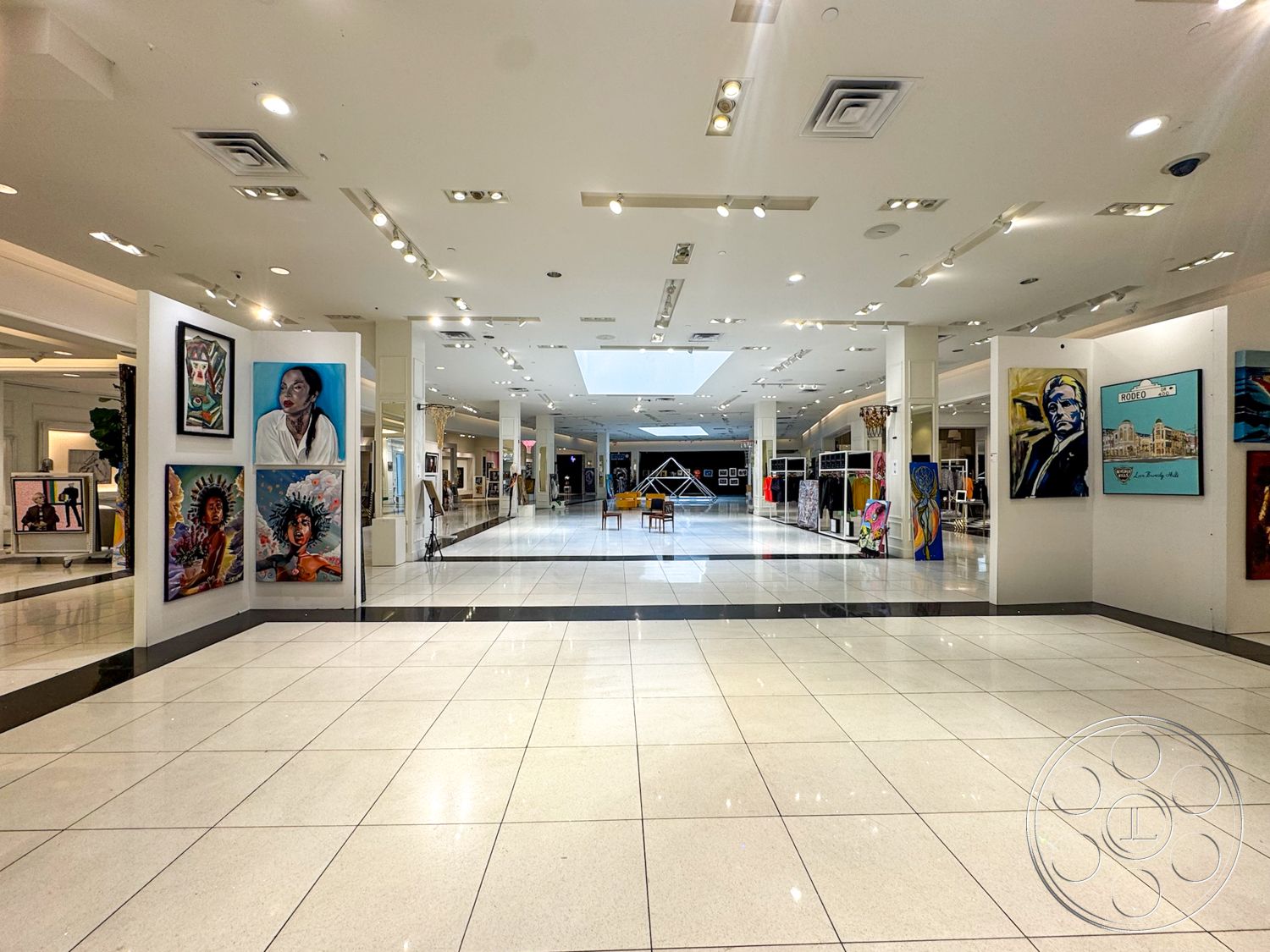 Beverly Gallery - exposed ceiling, white painted walls, track lighting fixtures, open hallway layout, polished porcelain tile flooring, large skylight, gallery-style wall panels, art display frames, modern art gallery style