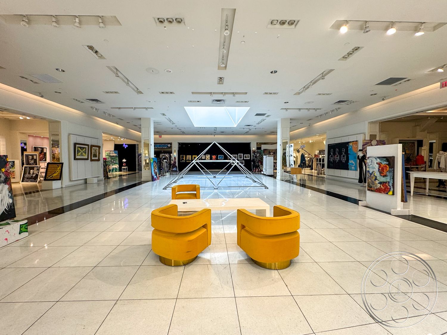 Beverly Gallery - high ceilings, neutral color palette, minimalist design elements, modern aesthetic, art display area, polished tile flooring, glass skylight, white painted walls, spotlight lighting, open gallery space, yellow curved seating, geometric sculpture