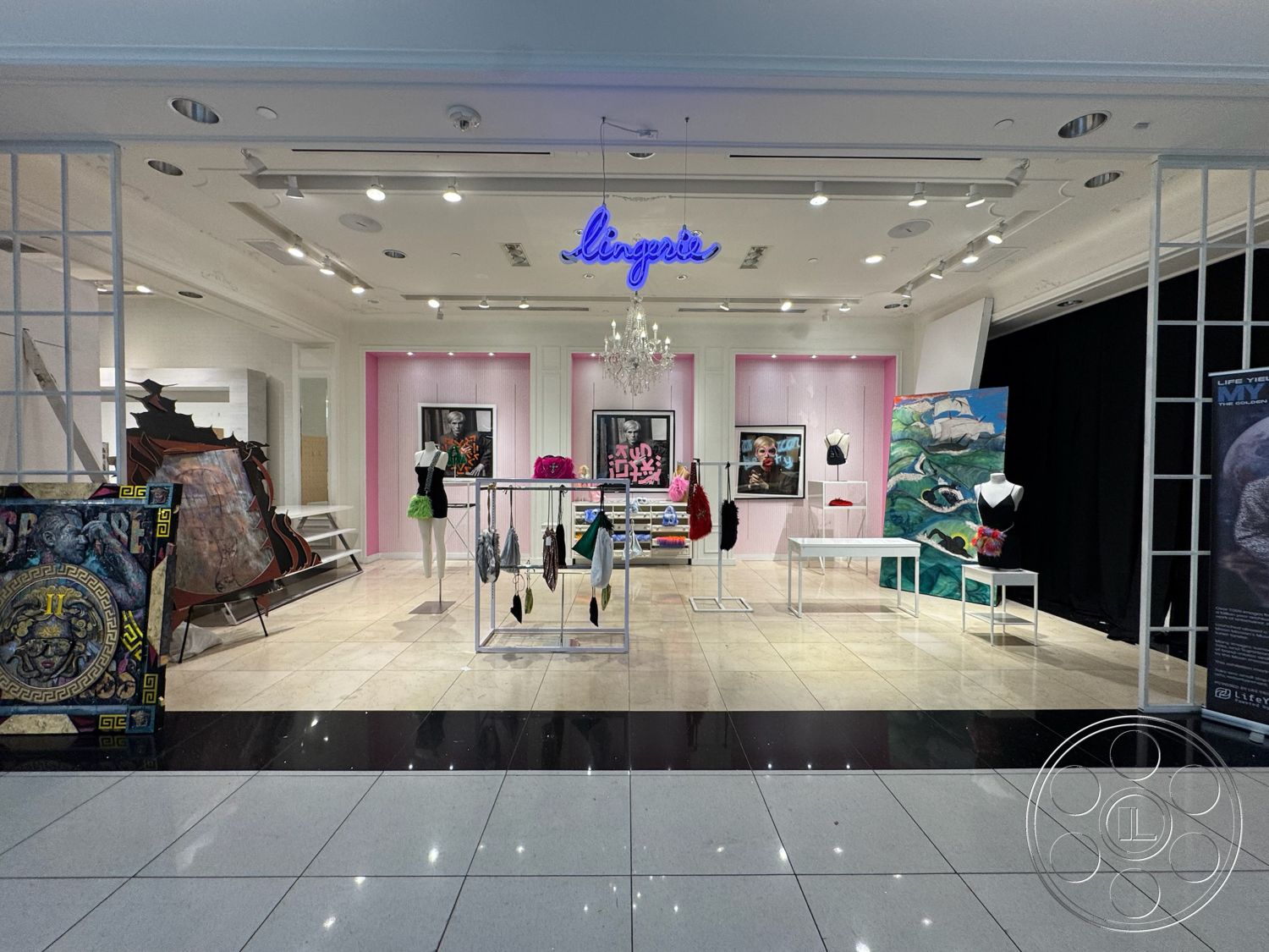 Beverly Gallery - decorative artwork, chandelier lighting, artistic installation, black accent wall, glass display cases, spotlight ceiling lights, clothing display racks, white drywall walls, polished ceramic tile flooring, pink feature wall, modern retail space, boutique shopping environment