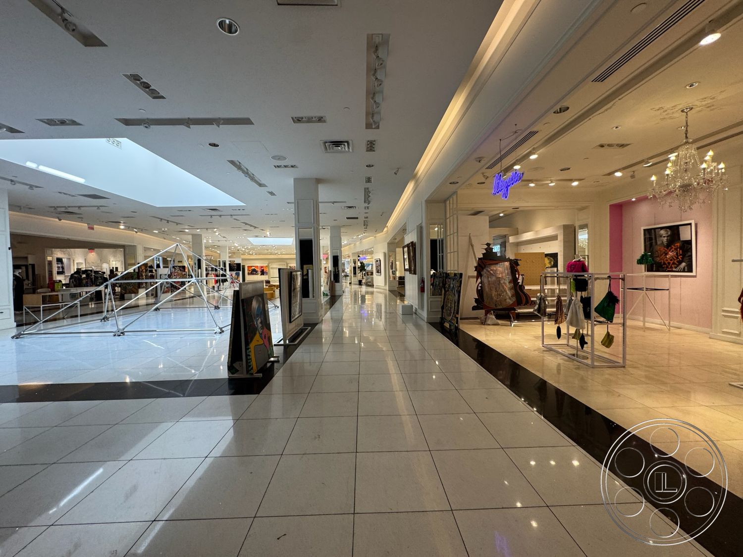 Beverly Gallery - high ceilings, neutral wall color, polished marble flooring, modern chandelier, glass skylight, exposed ceiling design, bright ceiling lights, open retail space layout, elegant display fixtures, storefront window displays, sleek black accent border, artwork display areas