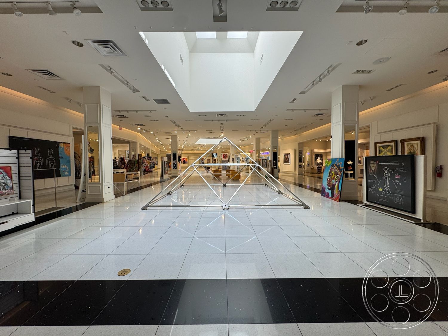 Beverly Gallery - open floor plan, high ceiling, art display area, polished tile flooring, glass skylight, white painted walls, exposed ceiling lights, black and white checkered tile pattern, minimalist exhibition space, modern geometric sculpture, accent walls for artwork display, clear acrylic display stands