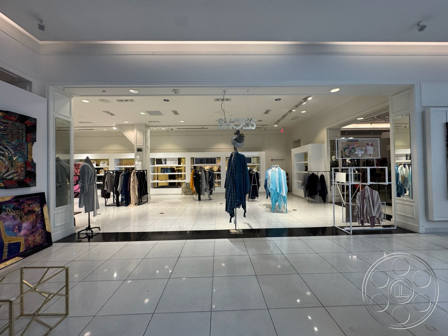 Beverly Gallery - neutral color palette, open layout, artistic wall decor, white painted walls, coffered ceiling details, bright overhead lighting, glass storefront, glossy white tile flooring, black accent tile flooring, modern retail store design, minimalist clothing display racks, stylish changing rooms