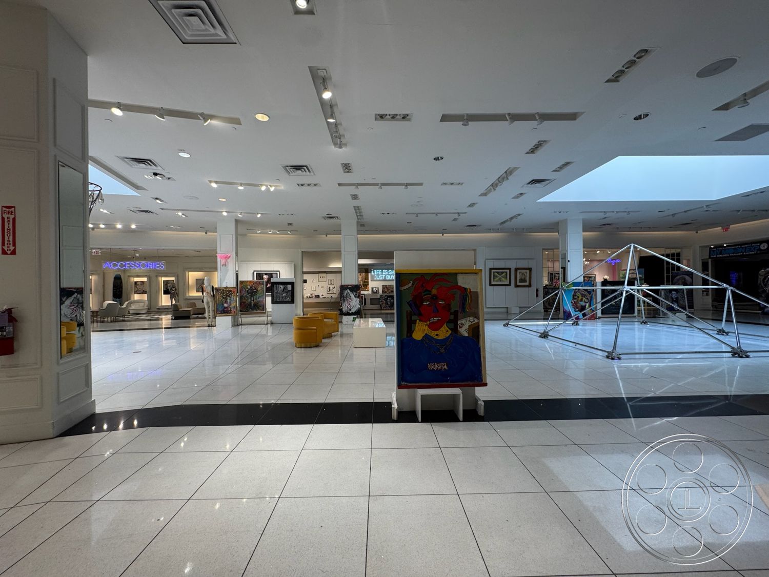 Beverly Gallery - polished tile flooring, white painted walls, skylight natural lighting, exposed ceiling lights, reception area with seating, high ceiling interior, modern art display area, open exhibition space, flush-mounted ceiling speakers, black accent tile border, fire extinguisher wall mounted, interactive art installation