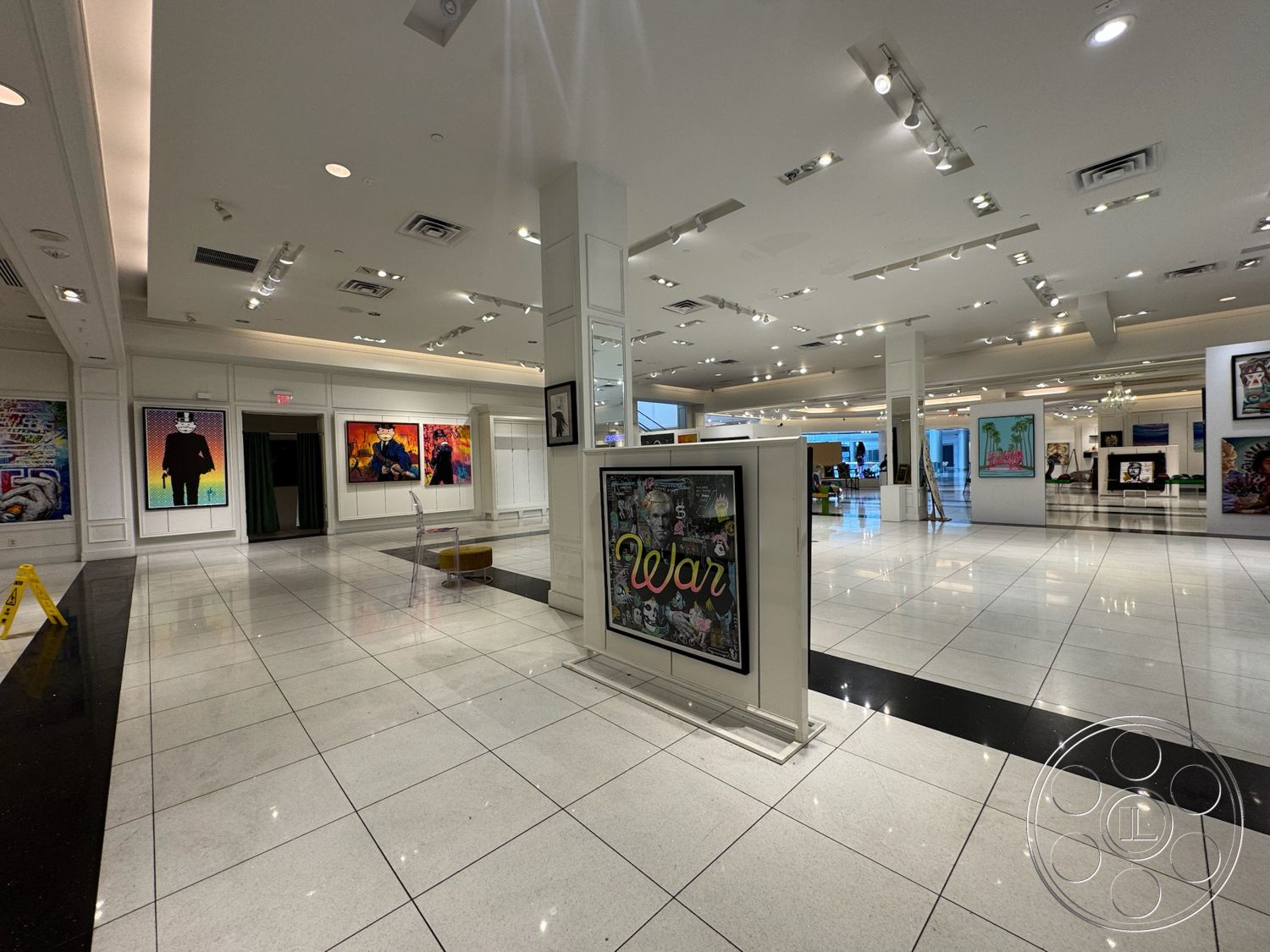 Beverly Gallery - high ceiling, white painted walls, spotlighting ceiling lights, modern art gallery, polished ceramic tile flooring, open exhibition space, black accent tile border, gallery style layout, framed artworks displayed on walls