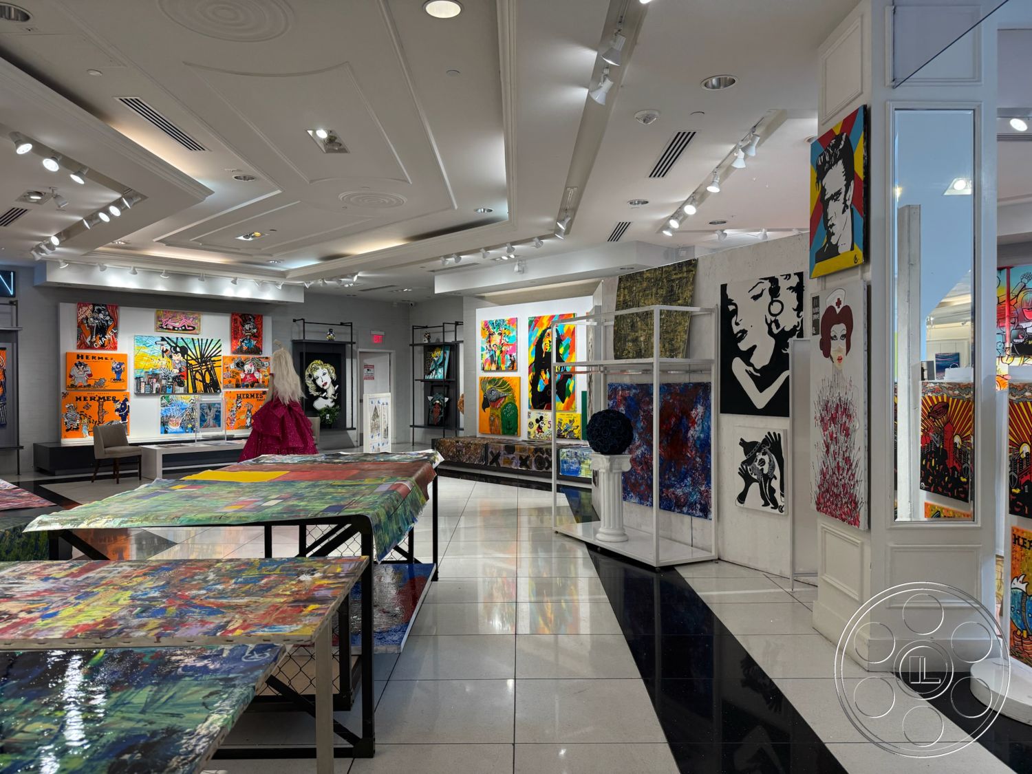 Beverly Gallery - open layout, minimalist architectural style, track lighting fixtures, interior art gallery, polished black and white tile flooring, modern drop ceiling with decorative detail, exhibition wall-mounted artwork, multi-colored abstract canvases, glass display pedestals, simple upholstered chairs, bright gallery lighting, raised display tables, vibrant wall colors