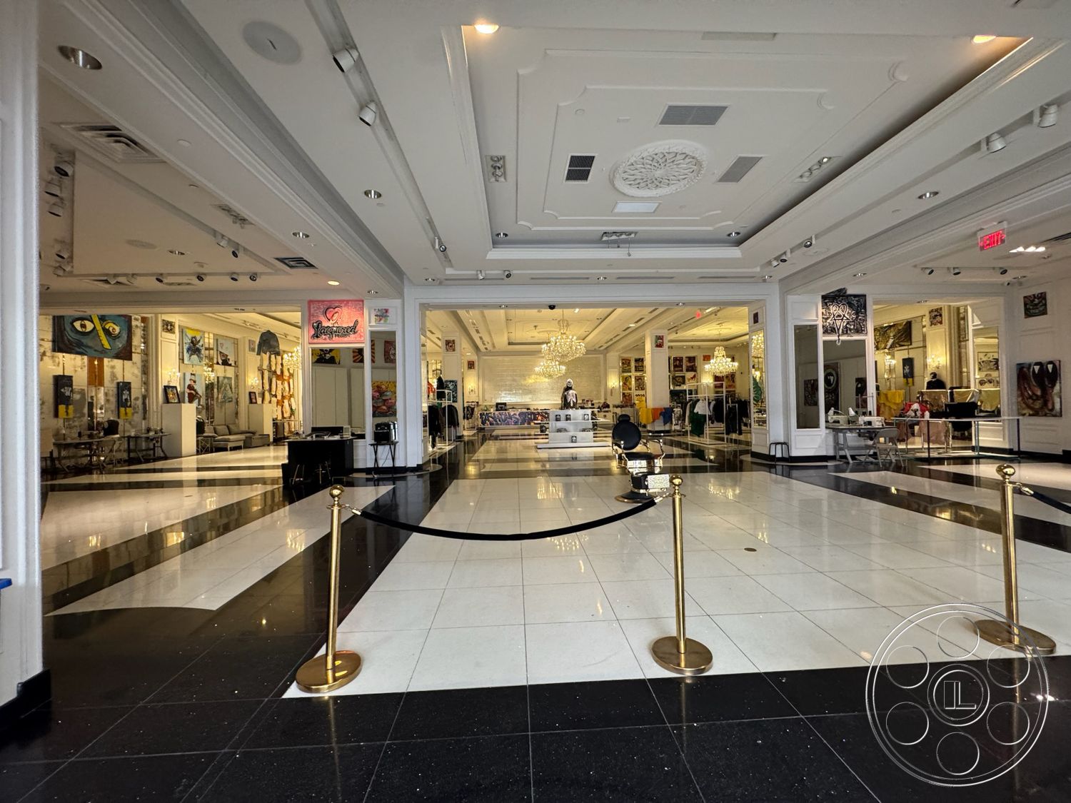 Beverly Gallery - coffered ceiling, open floor plan, polished marble flooring, art gallery setting, glass display cases, white painted walls, exposed ceiling details, decorative ceiling medallion, chandelier lighting fixtures, black and white checkered tile floor, interior exhibition space, gold stanchions with black velvet ropes