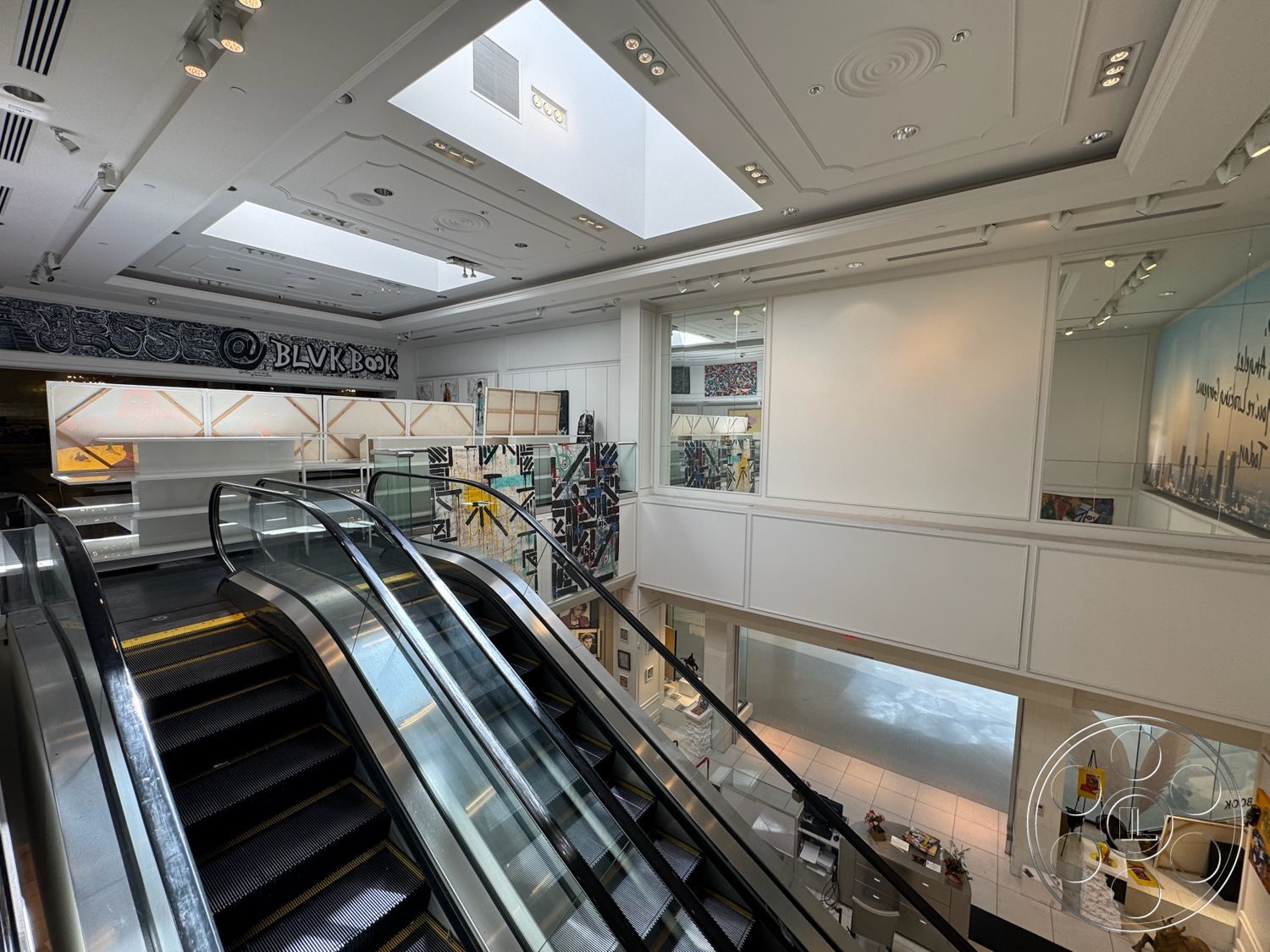 Beverly Gallery - tile flooring, contemporary lighting fixtures, white painted walls, skylight ceiling, modern retail environment, glass escalator, open atrium space, dropped ceiling with decorative molding, artwork wall displays