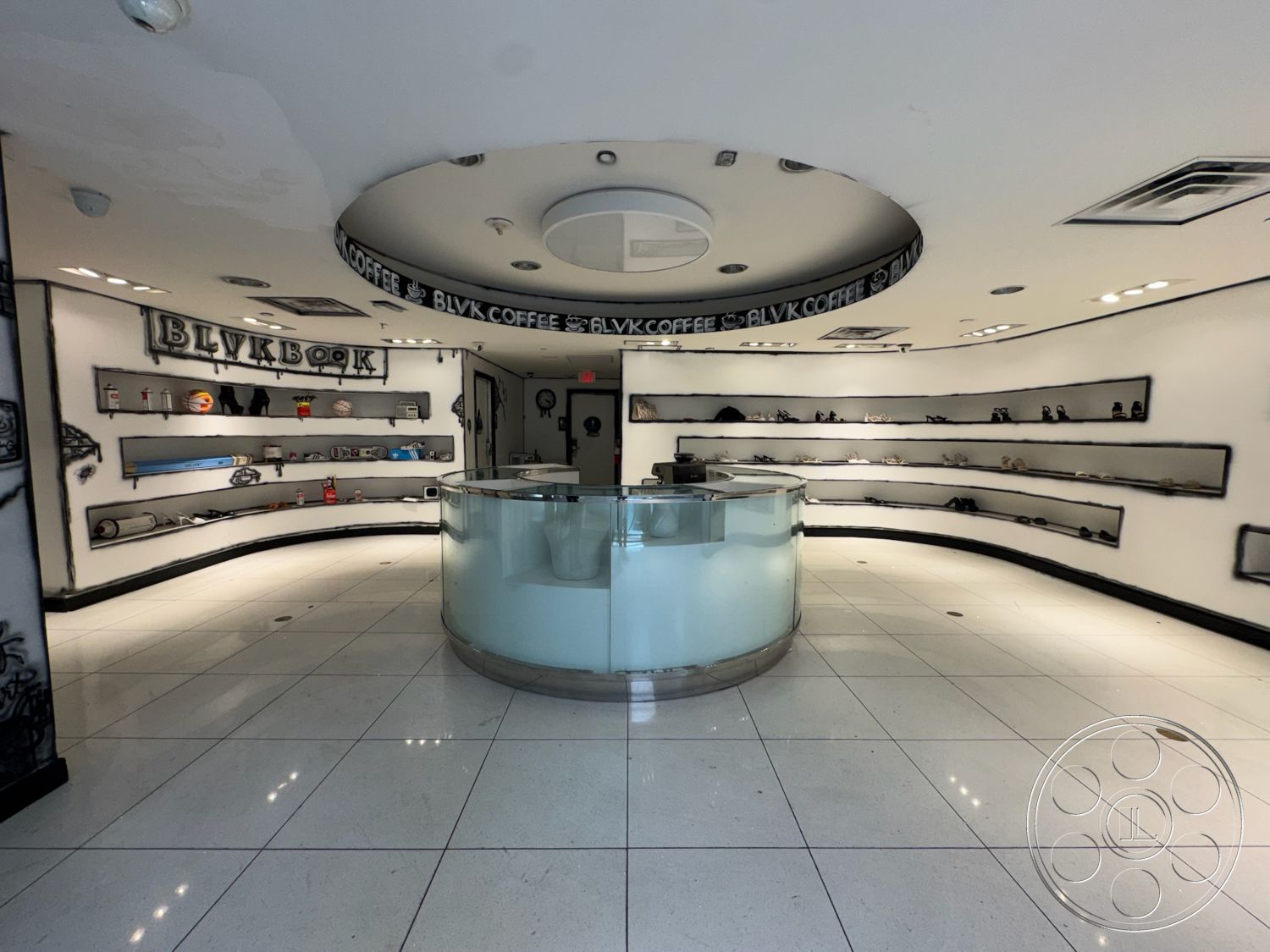 Beverly Gallery - polished tile flooring, open floor plan layout, white painted walls, minimalist architectural style, track lighting fixtures, contemporary retail space, curved glass reception desk, illuminated display shelves, ceiling with circular design