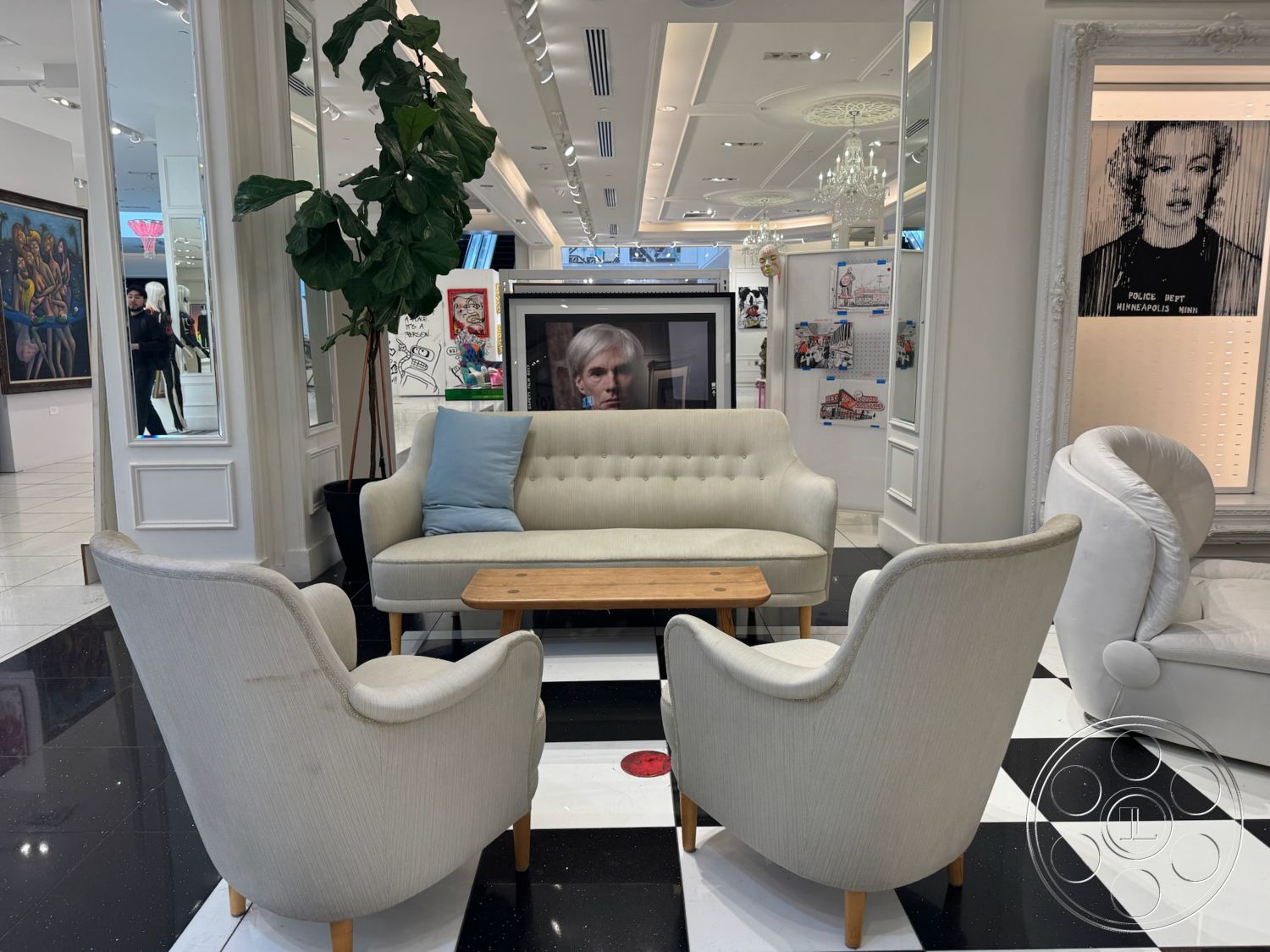 Beverly Gallery - neutral color palette, decorative indoor plant, natural wood coffee table, brightly lit environment, chandelier lighting fixtures, black and white checkered tile flooring, tufted fabric sofa, upholstered curved armchairs, mirrored wall panels, modern art gallery setting