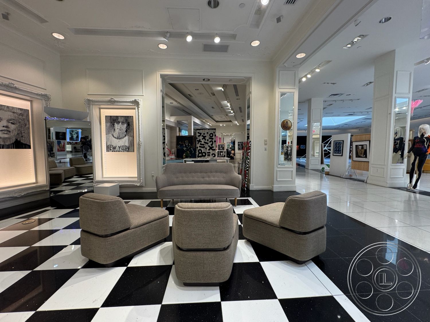 Beverly Gallery - high ceilings, contemporary furniture, black and white tile floor, open layout design, gray upholstered sofa, framed artwork on walls, decorative wall mirrors, modern ceiling lights, artistic display area, gray upholstered accent chairs, illuminated gallery space