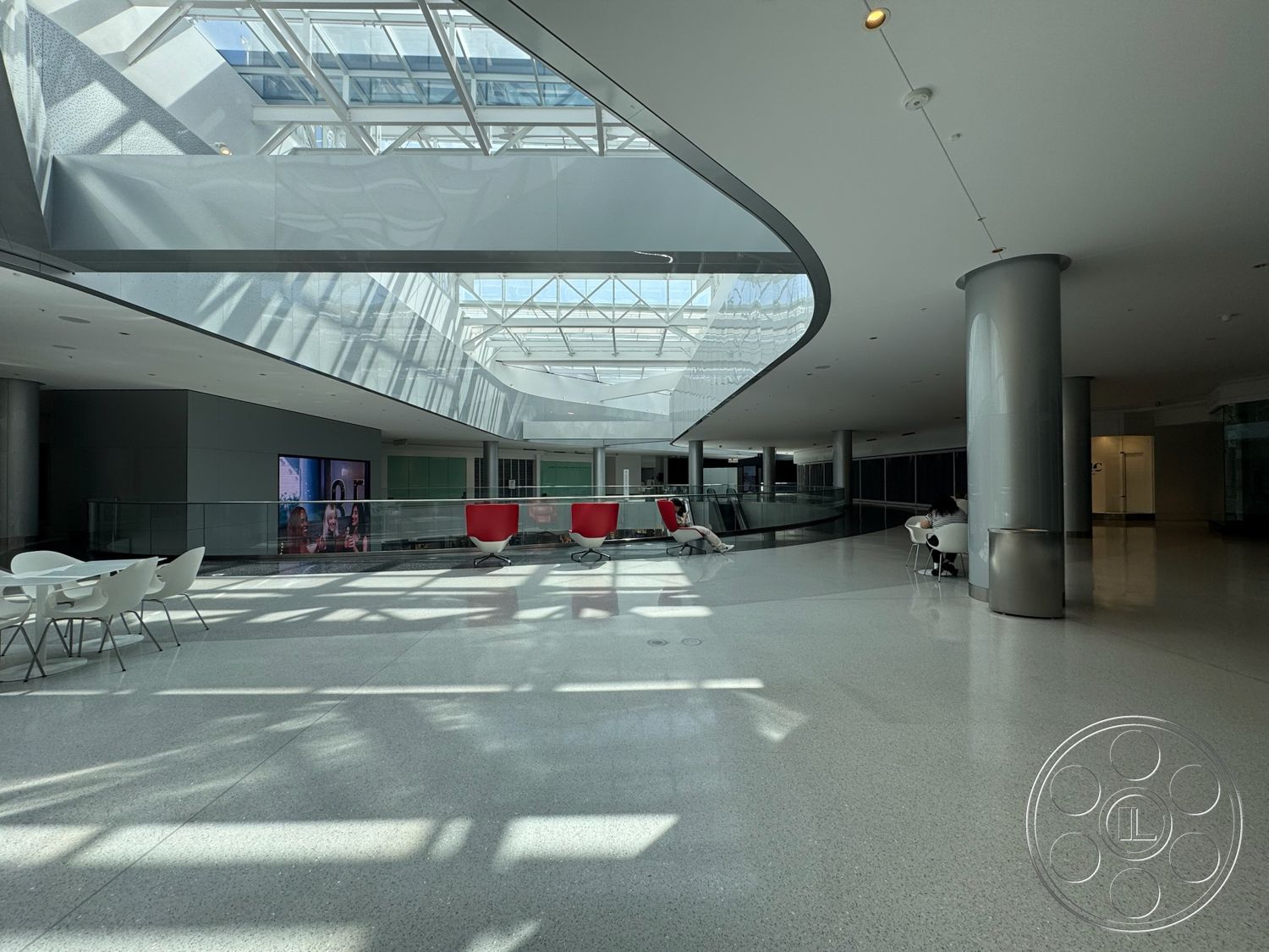 Beverly Gallery - open floor plan, bright natural lighting, contemporary design elements, polished terrazzo flooring, geometric lines, glass partition walls, minimalist architectural style, metal support columns, modern lounge seating, curved ceiling design, glass skylight feature