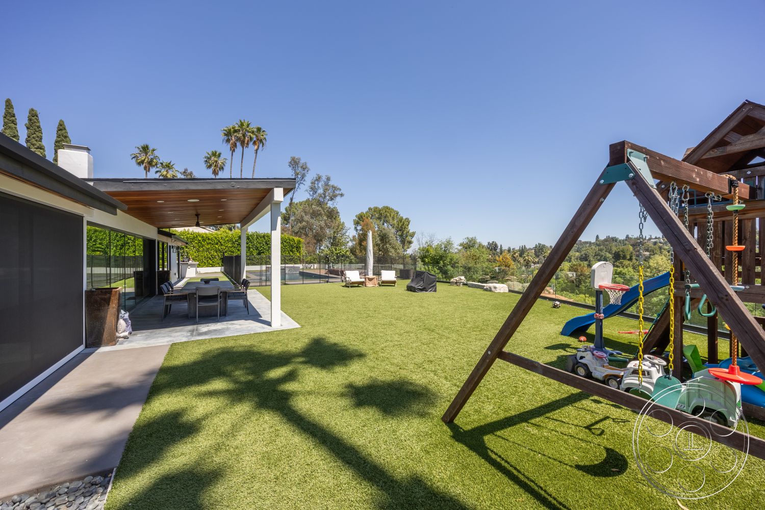 Modern 390 - exterior, landscaped garden, glass sliding doors, outdoor dining area, contemporary home, tropical palm trees, wood beam ceiling, concrete patio floor, artificial grass lawn, sunny suburban backyard, playground set, vacation-style setting