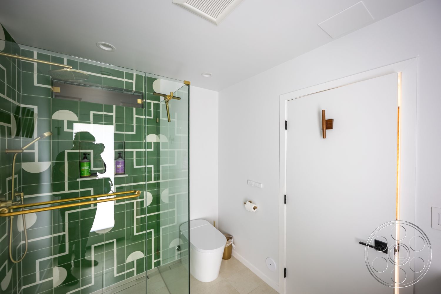 Modern 390 - minimalist bathroom design, white painted walls, modern toilet, stone bathroom flooring, transparent glass shower enclosure, textured green tile shower walls, golden brass shower fixtures, door with wooden handle, white bathroom door