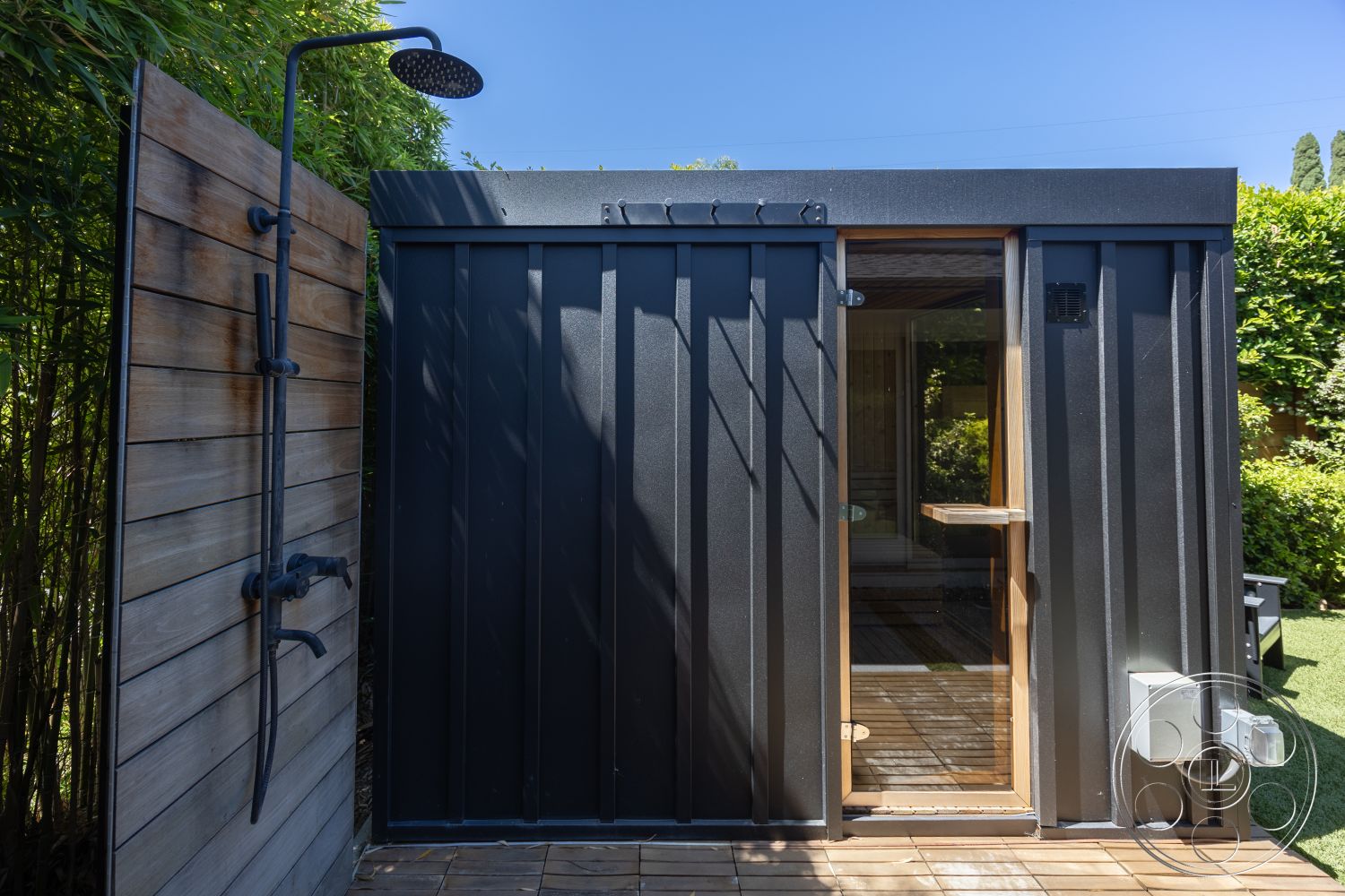 Modern 390 - exterior, landscaped garden, sliding glass door, minimalist architecture, flat roof design, cedar wood siding, metal wall paneling, wooden shower wall, black metal shower fixture, decking floor, modern outdoor shower, hidden drainage system