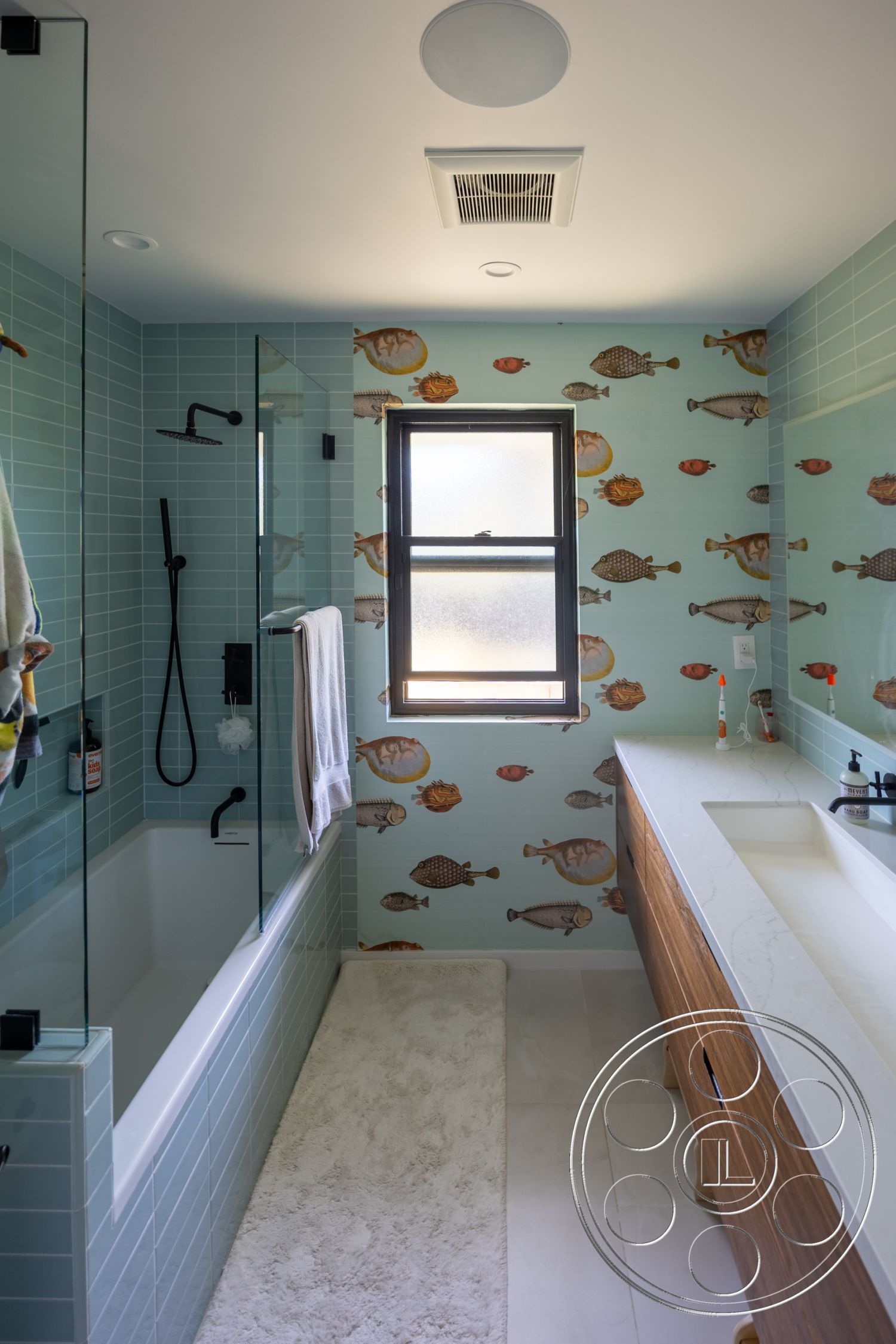 Modern 390 - glass shower enclosure, white marble countertop, recessed ceiling lights, interior bathroom, modern faucet fixtures, wood vanity cabinet, window with black frame, blue subway tile walls, animated fish wallpaper, white plush bath mat, bathtub with glass panel, square ceiling ventilation