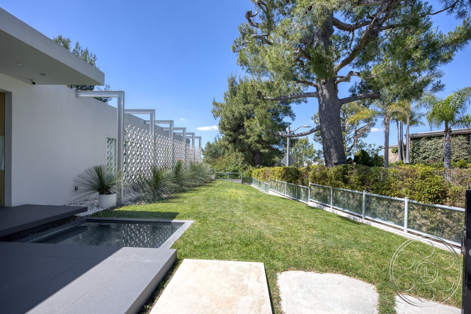 Modern 525 - exterior, white stucco walls, palm trees, natural sunlight, tall pine trees, glass sliding door, contemporary architectural style, decorative stone ground cover, landscaped garden with grass, modern concrete patio, grey concrete steps, opaque glass fence, vertical privacy screen