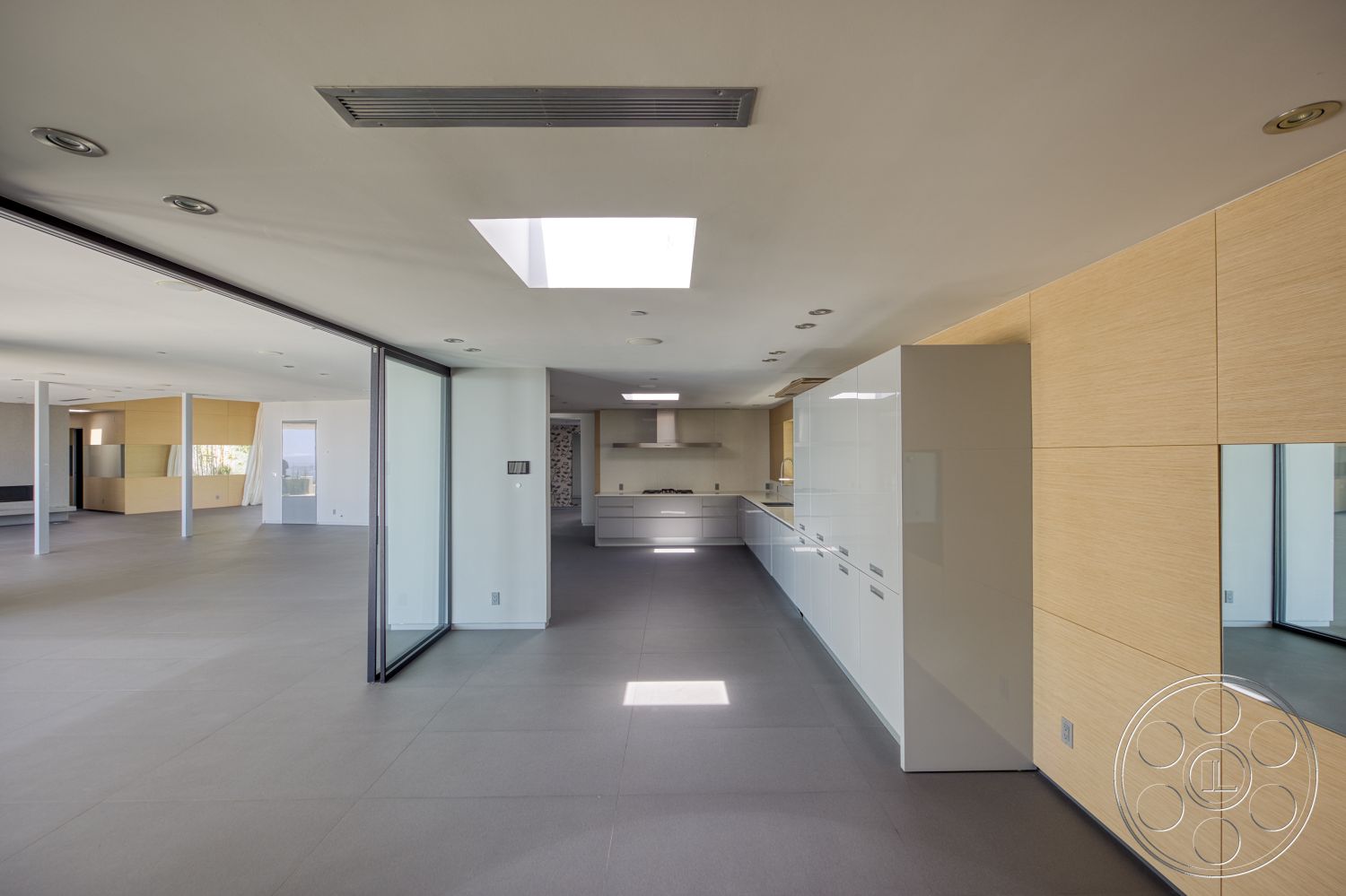 Modern 525 - neutral color palette, recessed lighting, minimalist design, open floor plan, concrete flooring, glass sliding doors, large open space, skylight, light wood wall paneling, white painted walls, steel structural columns, modern kitchen with glossy white cabinets